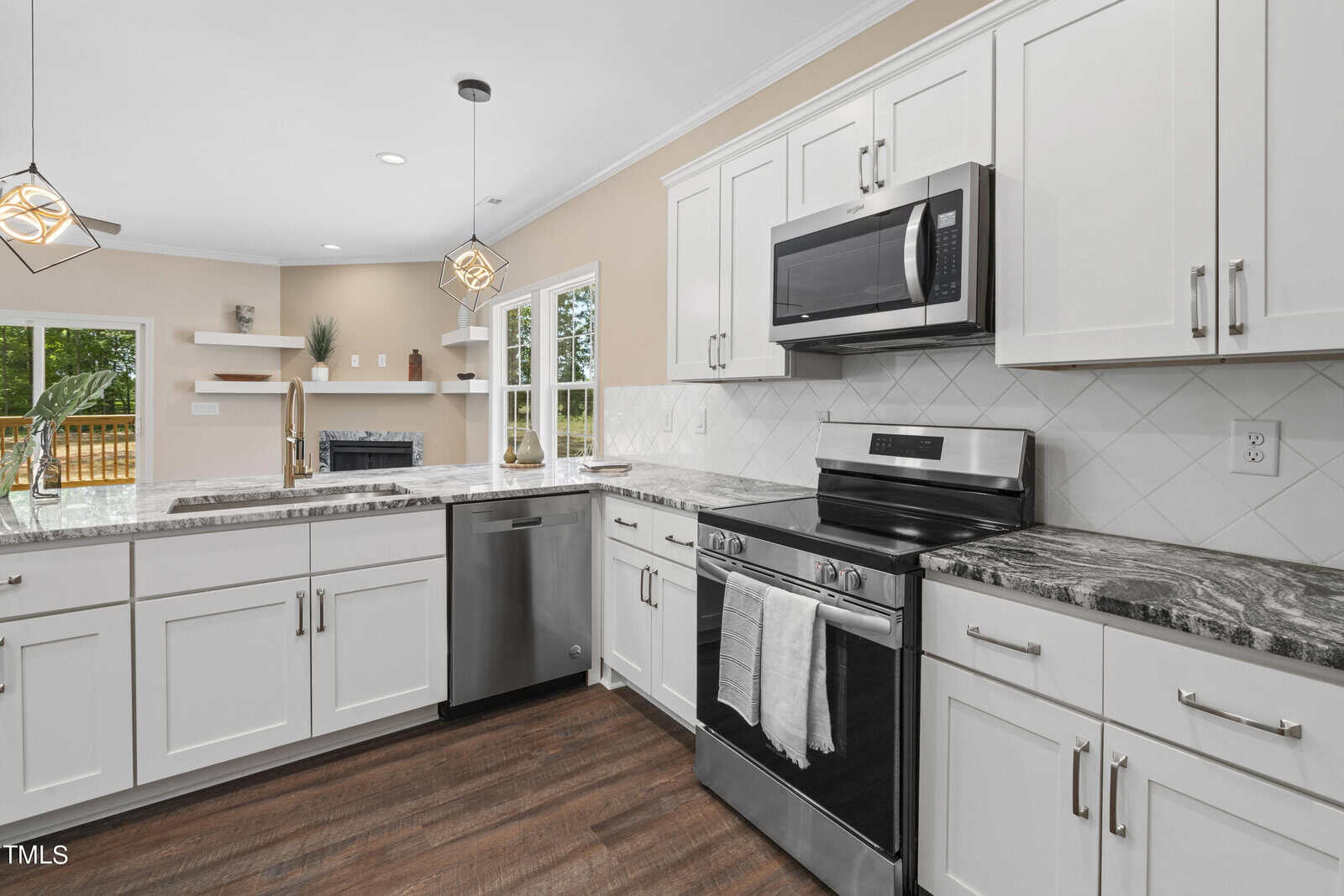 Modern kitchen with white cabinets, stainless steel appliances, marble countertops, and a dark wood floor. The space is bright with natural light from large windows and features pendant lights above the counter.