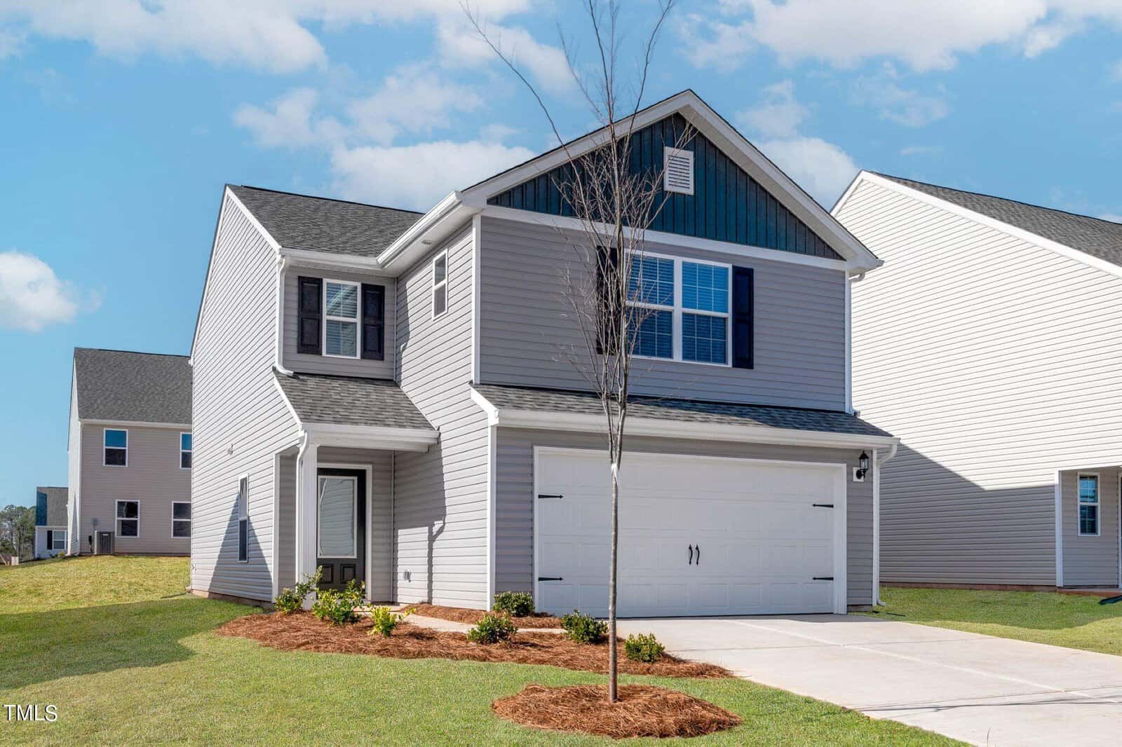 Located at 112 Cultivar Street in Oxford, this two-story modern house boasts gray siding, white trim, and a dark roof. It features a spacious white garage door and a small front lawn with a young tree under the clear sky.