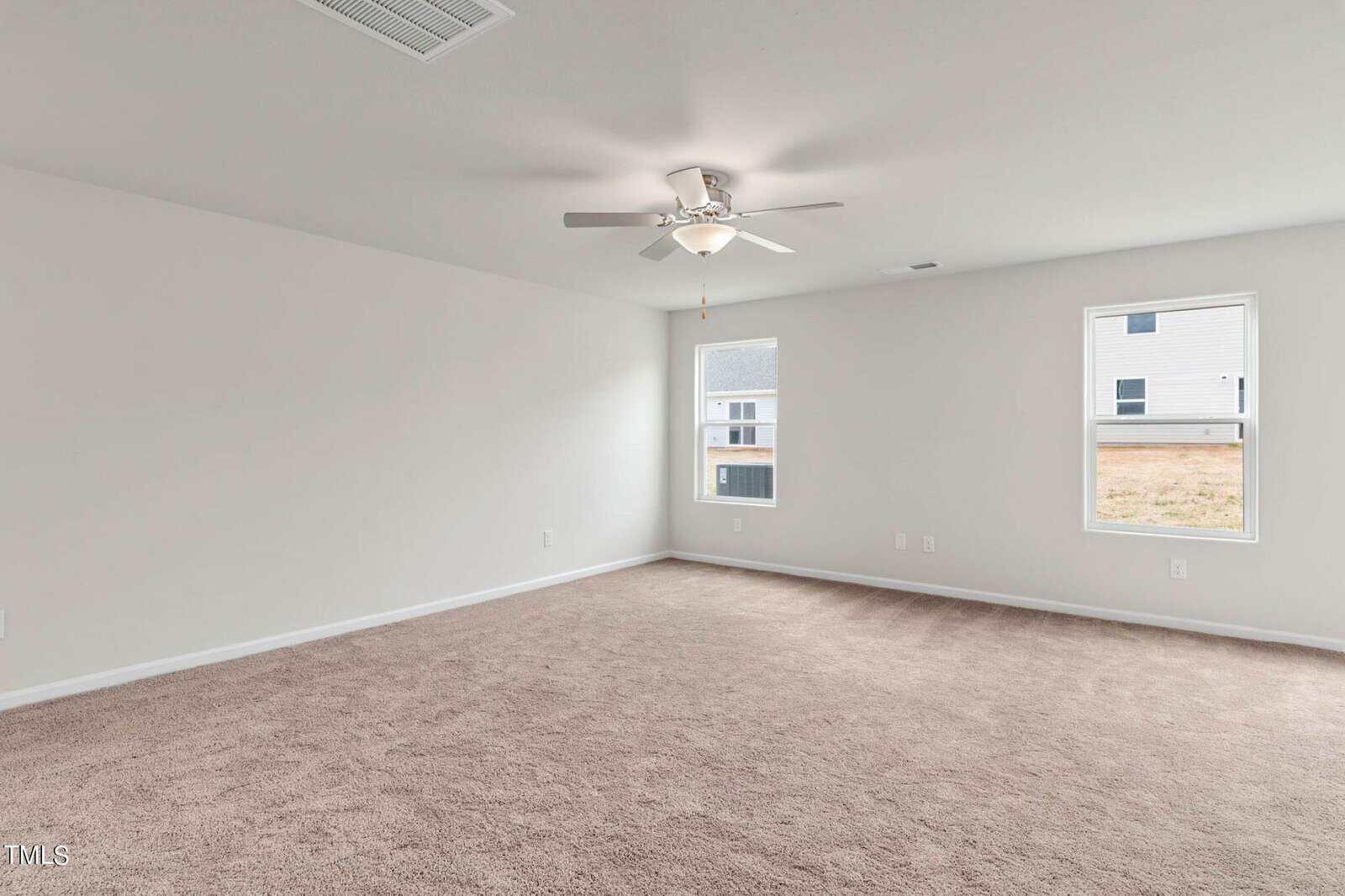 Spacious empty room with beige carpet, white walls, and a ceiling fan. Two windows bring natural light into the space.