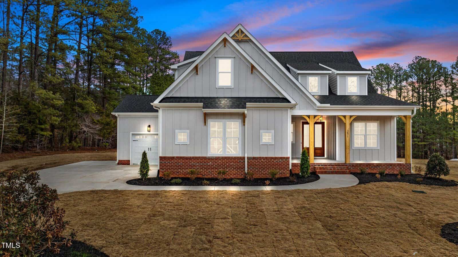 Set against a vibrant sunset sky, this modern gray two-story house at 3671 Graham Sherron Road, Wake Forest, boasts a brick foundation and white trim. Neatly trimmed grass and shrubs grace the front yard, while a driveway leads to the attached garage on the left.