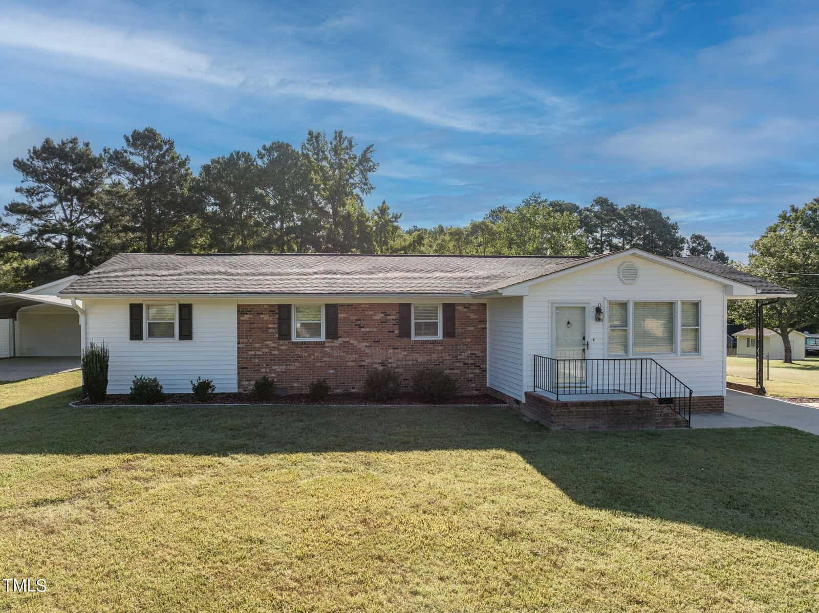 The single-story house at 814 N Crescent Drive in Creedmoor boasts white siding and a charming brick facade. A welcoming front porch with steps descends to a lush, grassy lawn, while trees stand gracefully in the background beneath the clear blue sky.