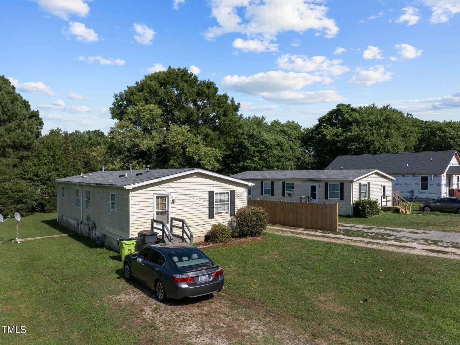 A small residential area on 126 Daniel Street in Oxford features a beige mobile home with a black car parked in the driveway. Adjacent homes and a wooden fence are visible, against a backdrop of green trees and a partly cloudy sky.