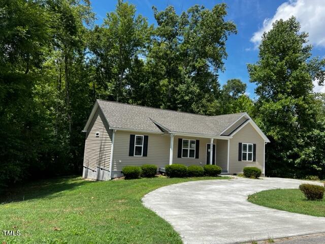 Nestled on 2557 Mint Julep Drive, this charming single-story beige house in Creedmoor features dark shutters and a cozy porch. A circular driveway welcomes you, surrounded by lush green trees and neatly landscaped bushes. The partly cloudy sky adds to the serene ambiance of the front yard.