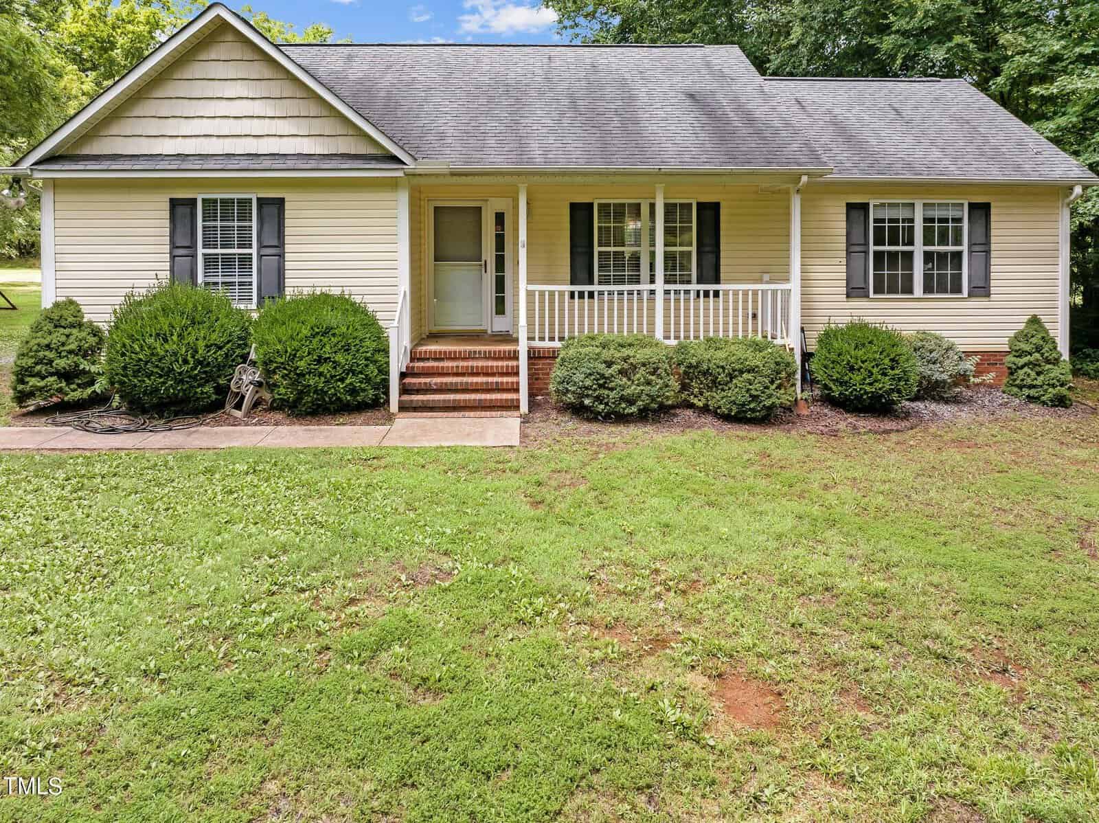 Nestled at 2162 Smith Road, this charming one-story house in Oxford boasts beige siding and a dark gray roof. It features a covered front porch with white railings and brick steps. The grassy front yard is bordered by lush shrubs and trees, creating a serene haven.