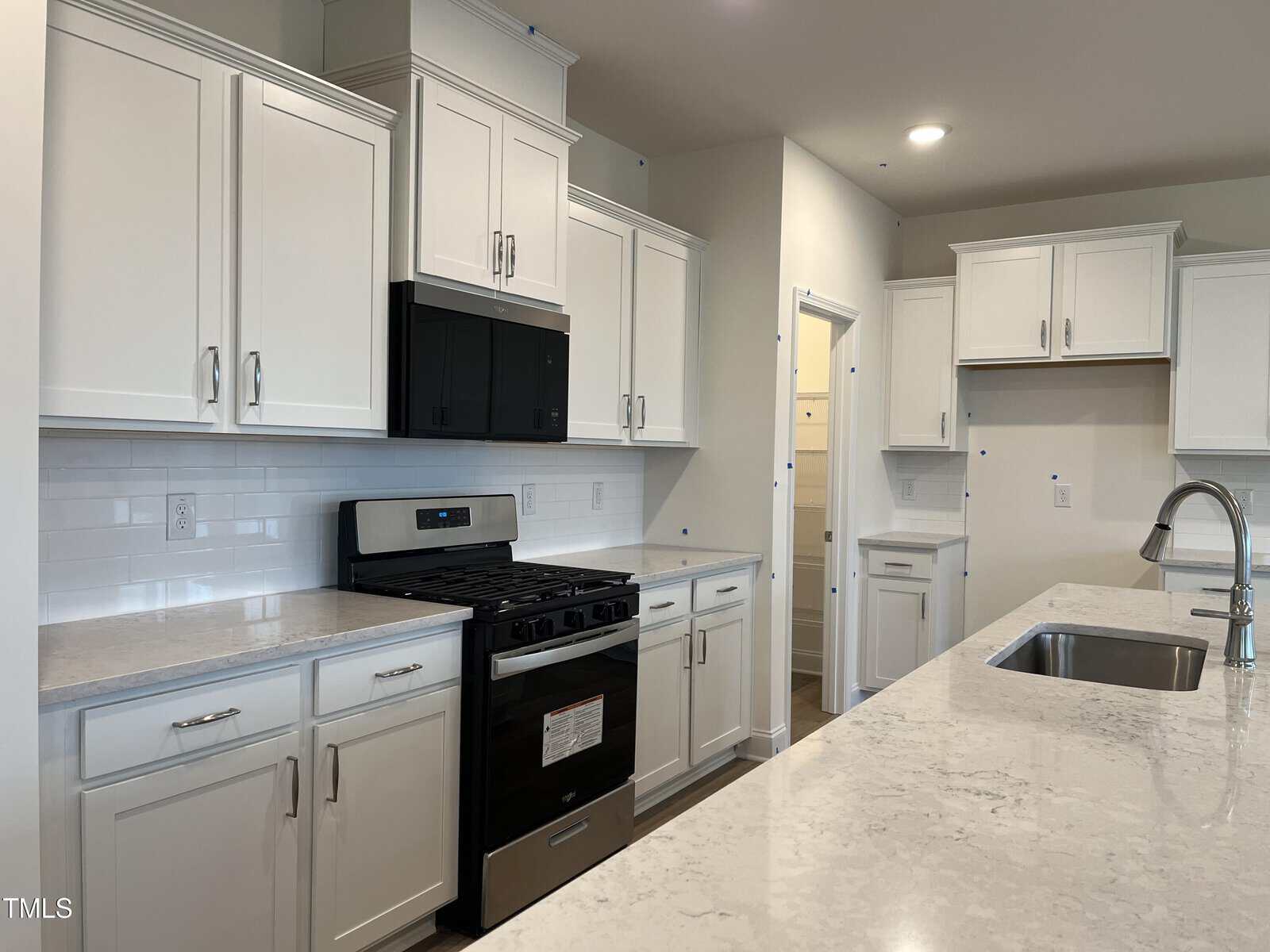 Modern kitchen with white cabinets, stainless steel gas stove, built-in microwave, white tile backsplash, and a marble island countertop with a sink. Recessed lighting brightens the room.
