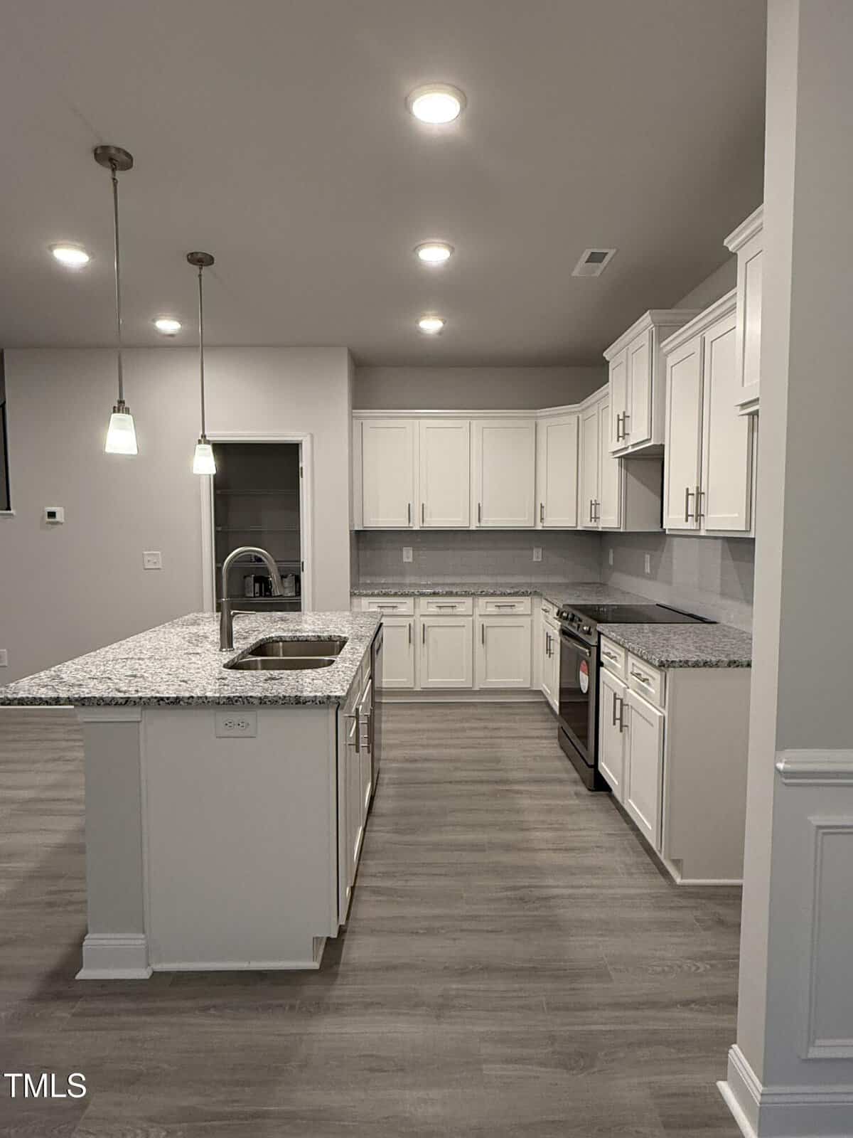 Modern kitchen with white cabinets, gray granite countertops, a center island with a sink, stainless steel appliances, pendant lights, and light wood flooring. The space is well-lit with recessed ceiling lights.