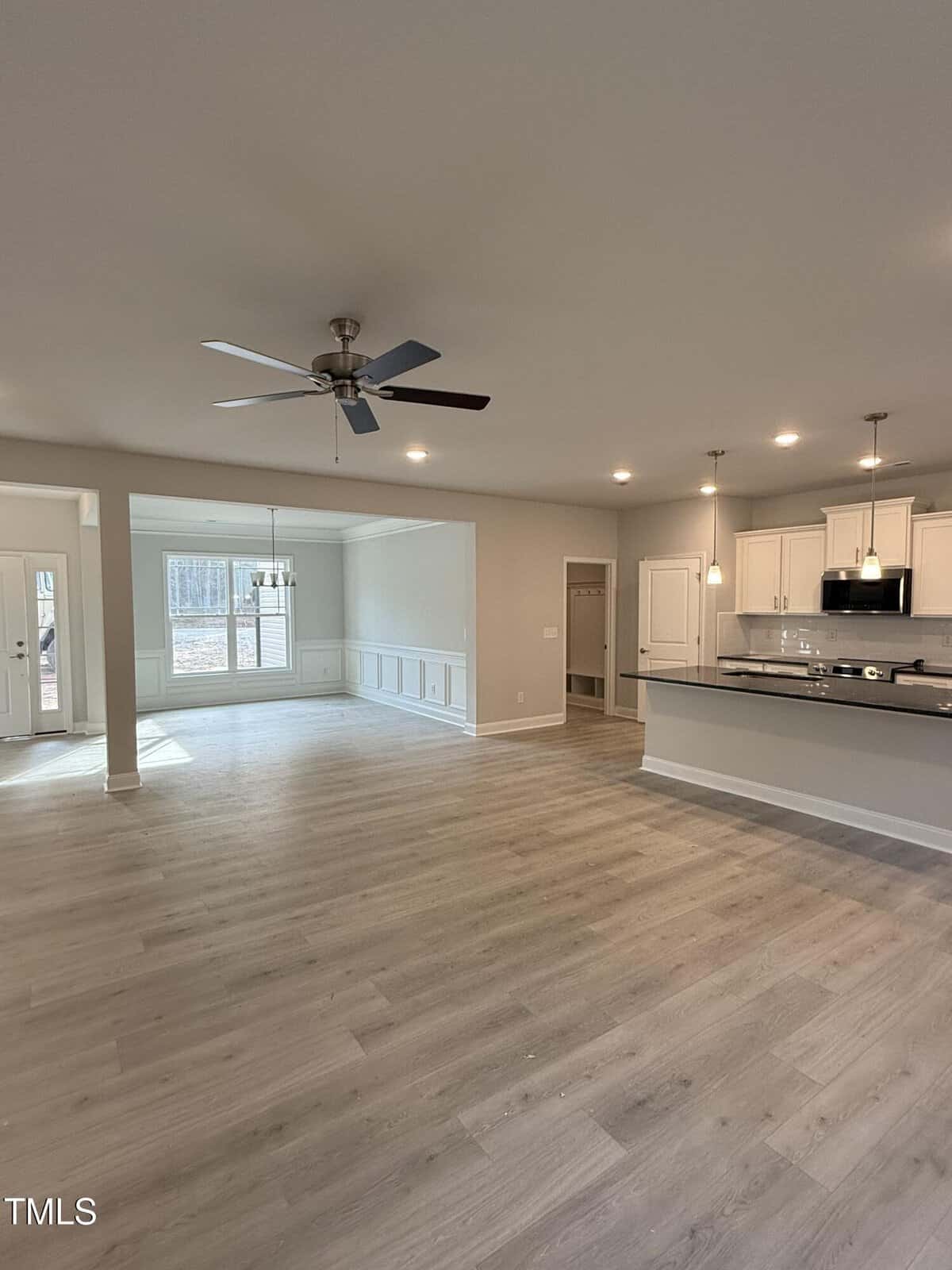 Spacious, modern open-concept kitchen and living area with light wood floors, white cabinets, a ceiling fan, recessed lighting, and large windows letting in natural light. Dining area visible in the background.
