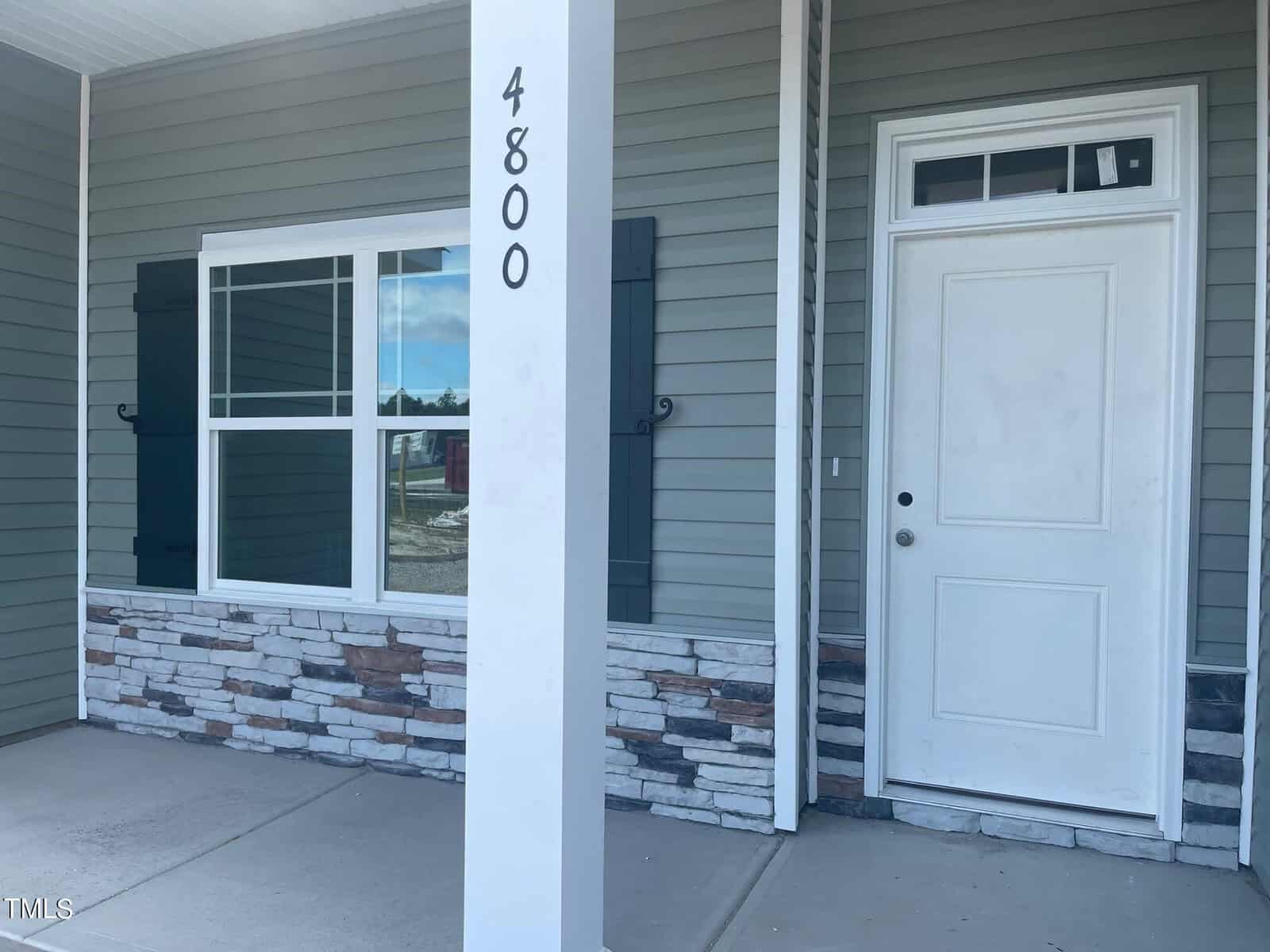 A white front door and window with dark green shutters on a house with gray siding and partial stone facade. The porch post displays the house number 4800 in black vertical text.