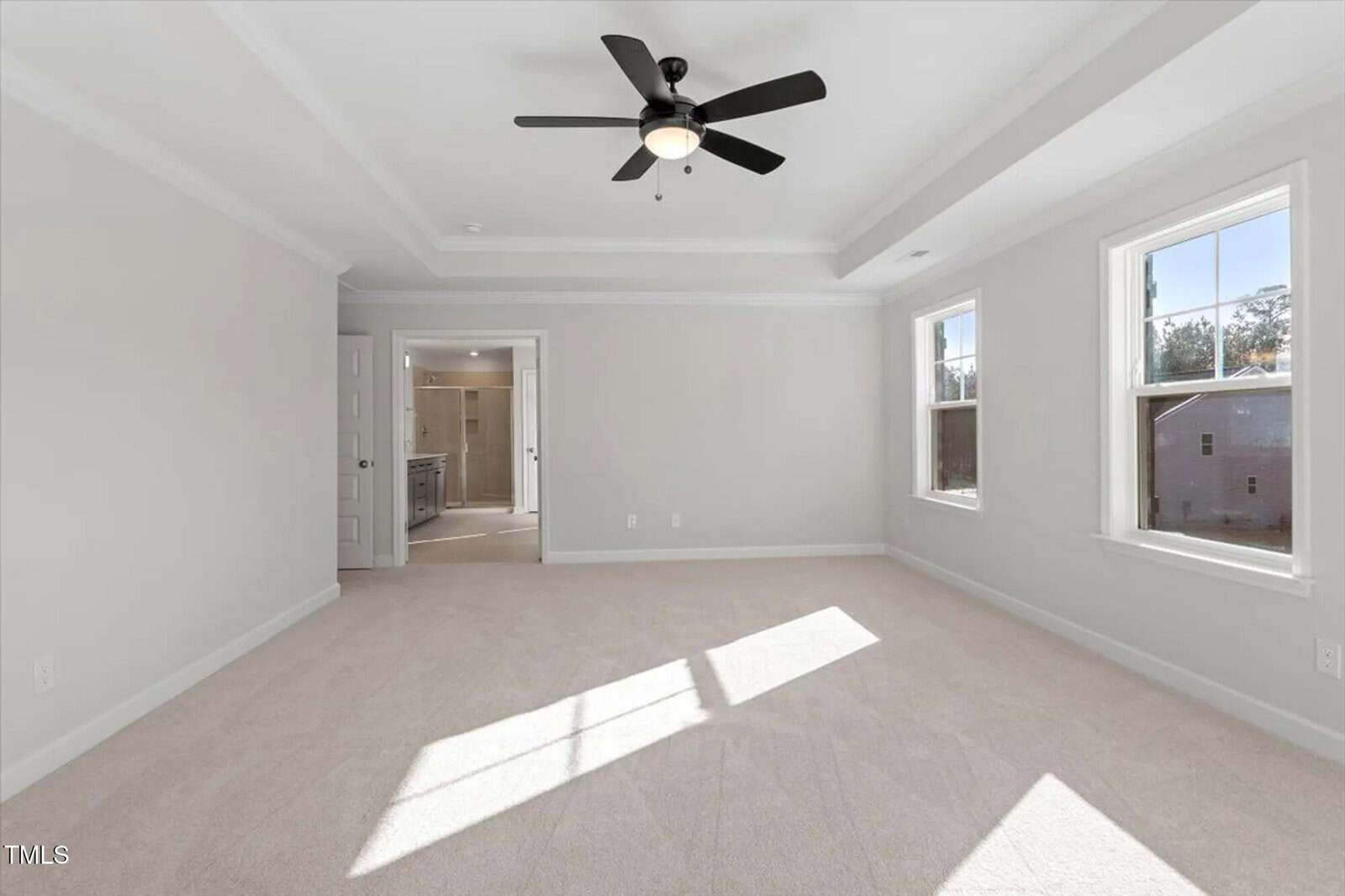 Empty bedroom with light beige carpet, gray walls, two windows, a black ceiling fan with light, and an open door leading to a bathroom. Sunlight streams onto the floor from the windows.
