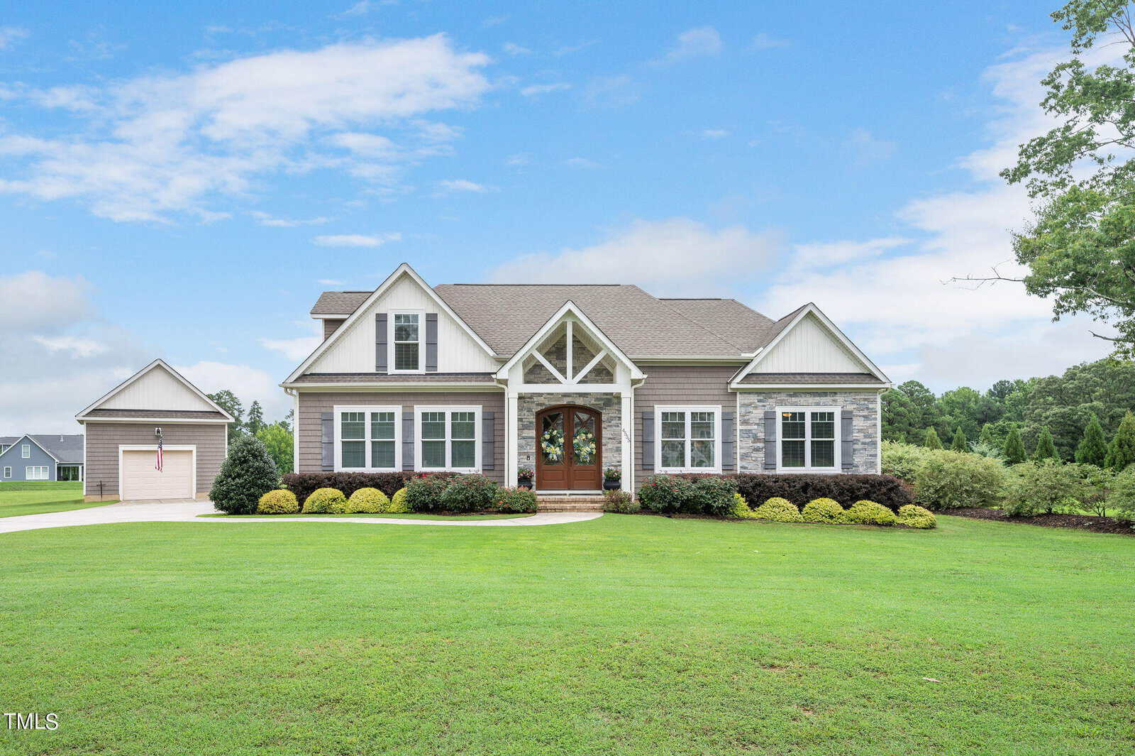 A suburban house on 4555 Austins Lane in Franklinton features a well-maintained lawn, gray siding, and stone accents. It boasts a gabled roof and a welcoming porch with a brown double door. A two-car garage sits to the left, framed by trees and a partly cloudy sky.