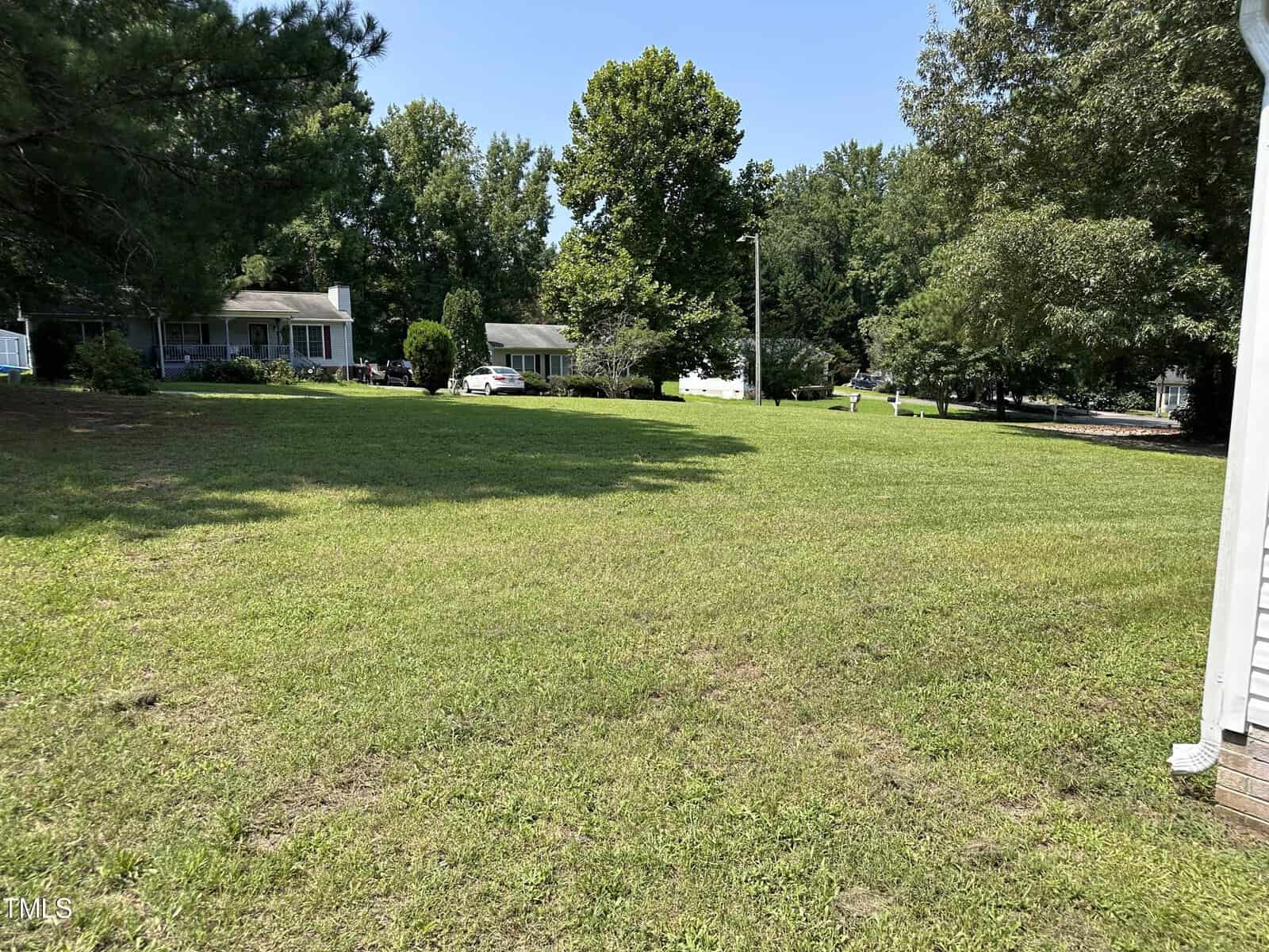 A grassy lawn with scattered trees, bordered by a few suburban houses under a clear blue sky.