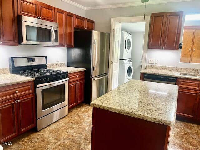A modern kitchen with stainless steel appliances, including a gas stove and refrigerator. Cherry wood cabinets and granite countertops are featured throughout. A laundry area with a stacked washer and dryer is visible through a doorway.