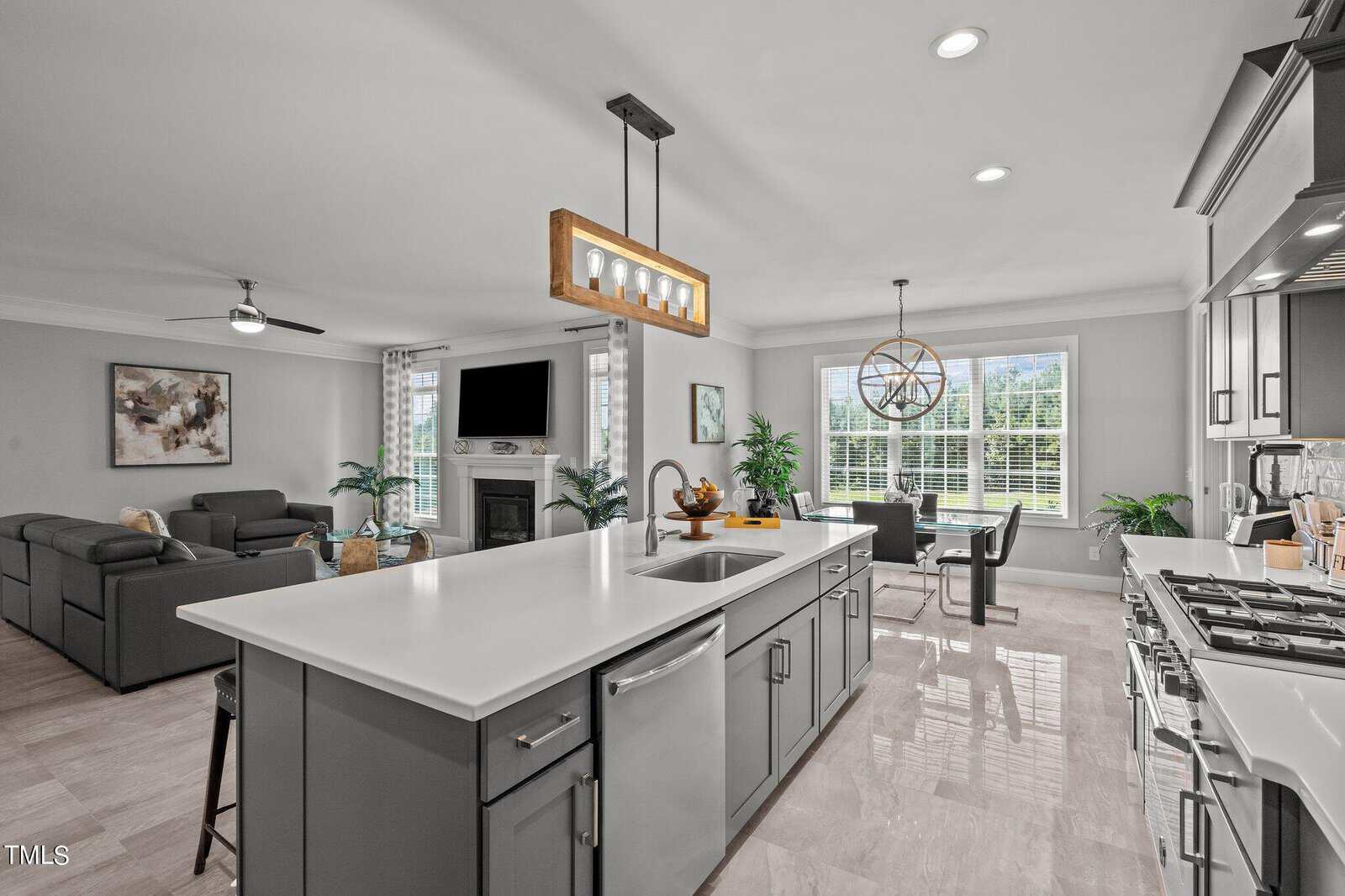 Modern open-concept kitchen with gray cabinets, white countertops, a large island with sink, stainless steel appliances, and adjacent living and dining areas with large windows and contemporary decor.