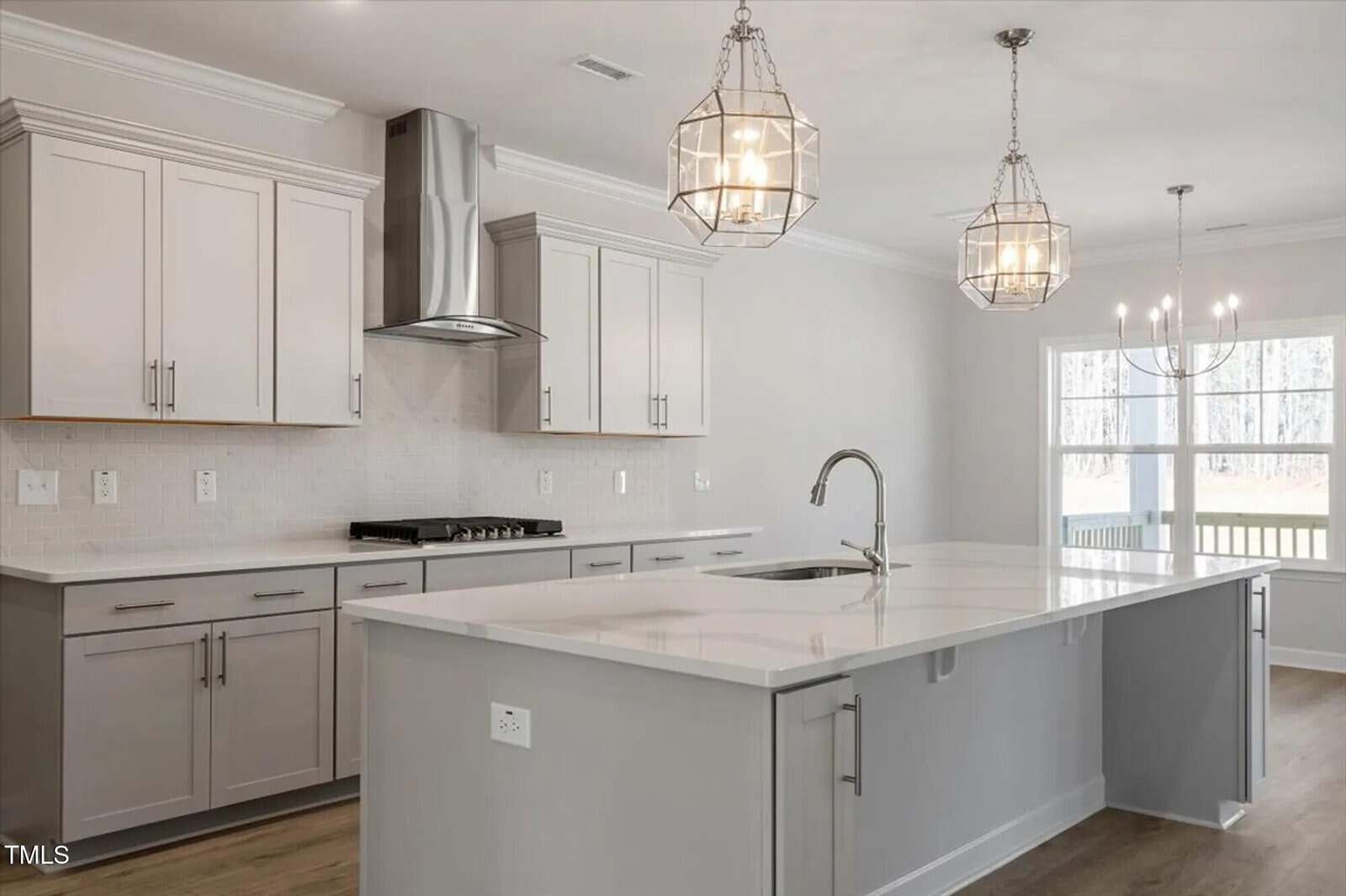 Modern kitchen with light gray cabinets, stainless steel appliances, a large white marble island with a built-in sink, two pendant lights above the island, and a large window in the background.