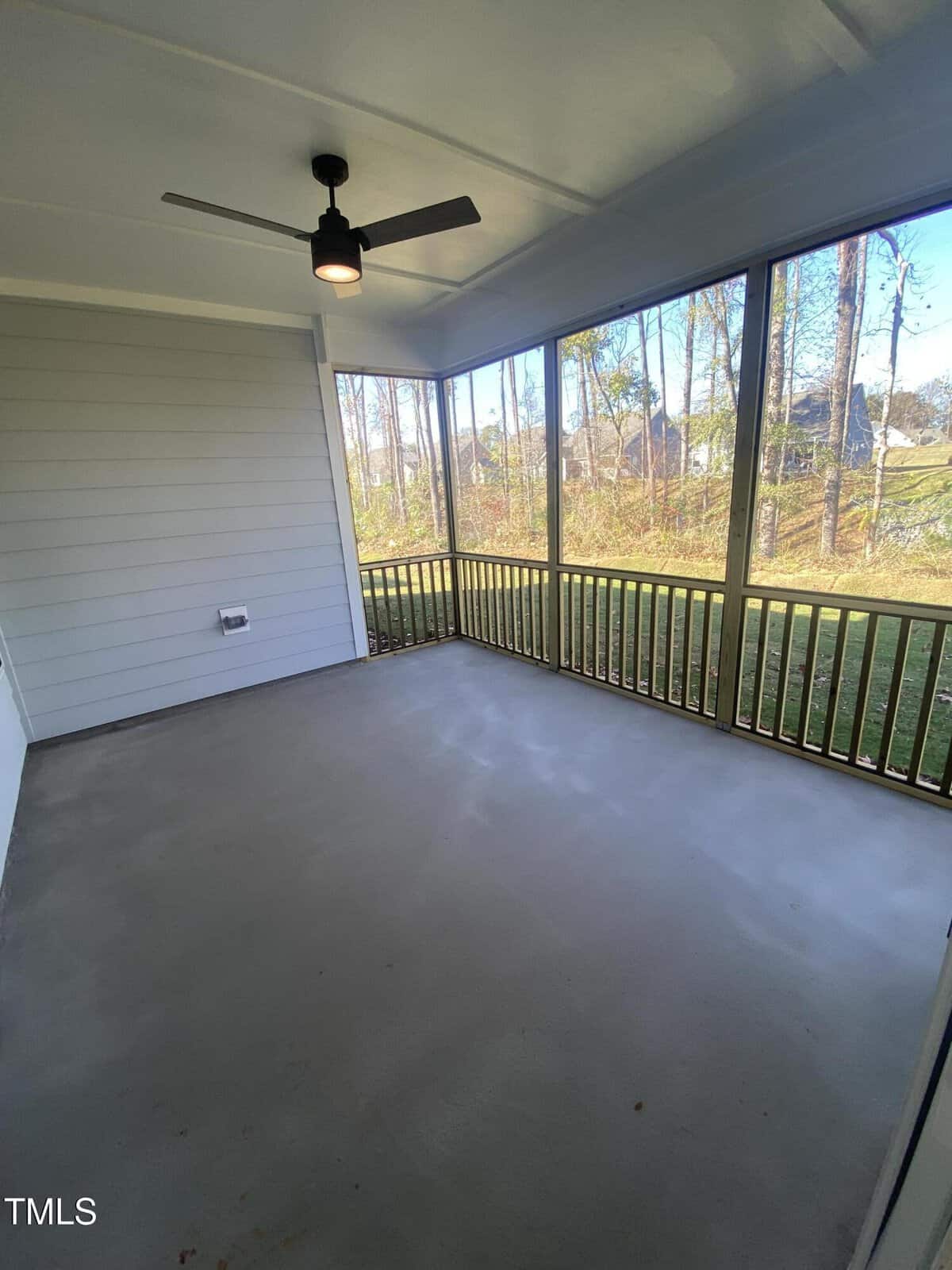 Screened-in porch with a ceiling fan, gray flooring, light-colored siding, and large screened windows overlooking a grassy yard and trees.