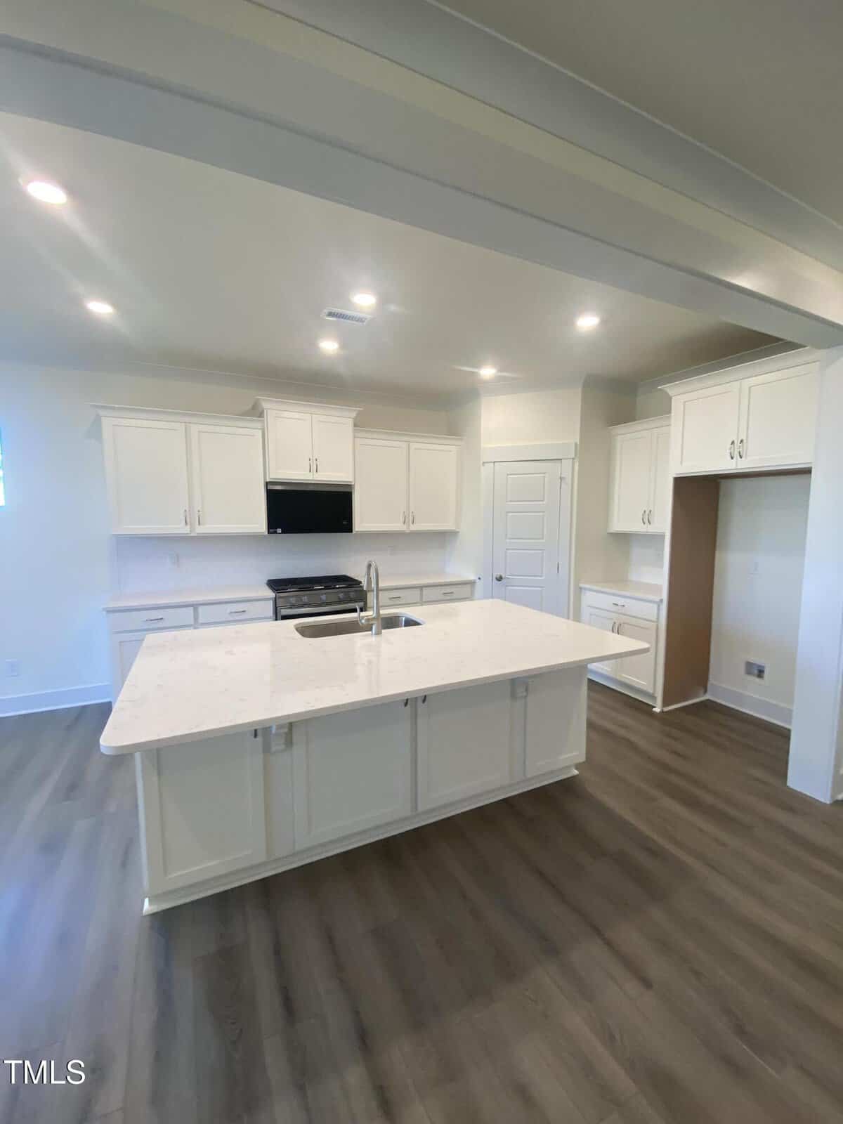 A modern kitchen with white cabinets, stainless steel appliances, a large white island with a sink, and wood-style flooring under bright recessed lighting.