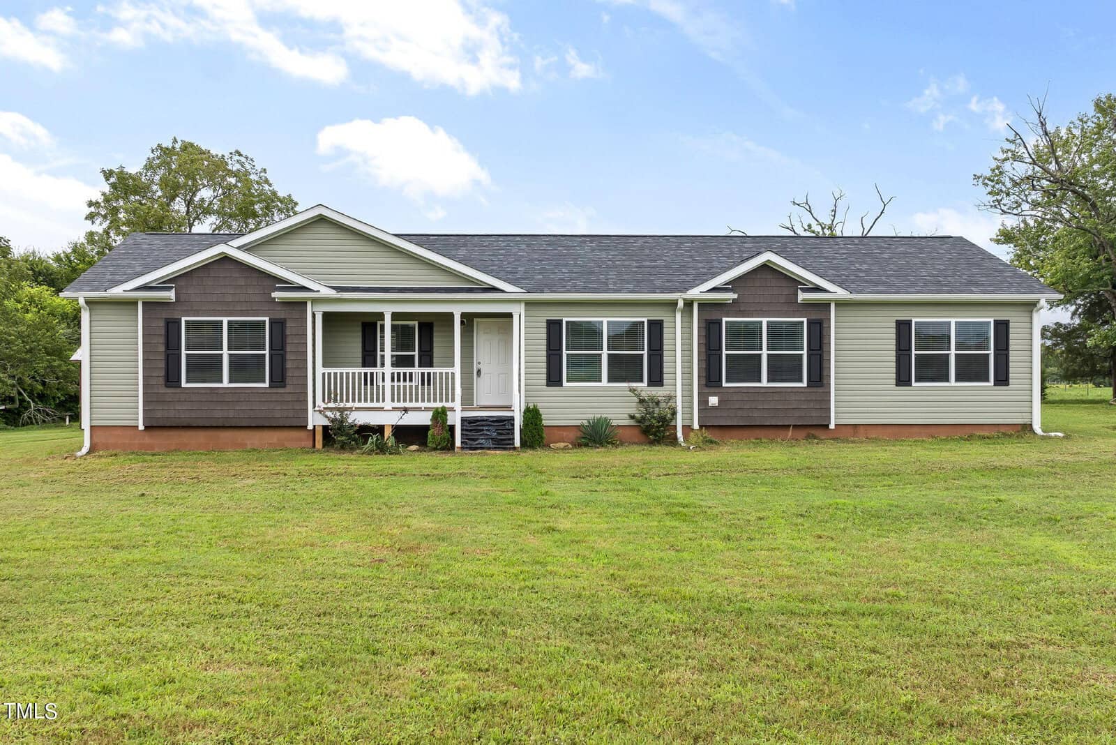 Single-story house with gray and white exterior, a front porch with white railings, a dark shingled roof, and a well-kept lawn at 261 Sollie Ayscue Road. The overcast sky and trees in the background suggest a serene and rural setting in Henderson.