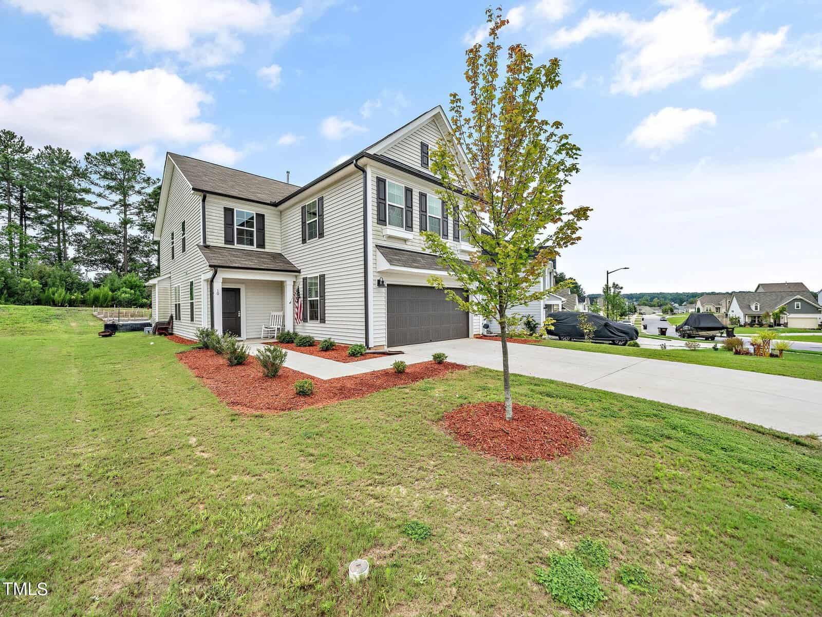 A two-story modern house with gray siding and black shutters, a double garage, manicured lawn, a tree in mulch, shrub landscaping, and a wide driveway on a corner lot in a suburban neighborhood.