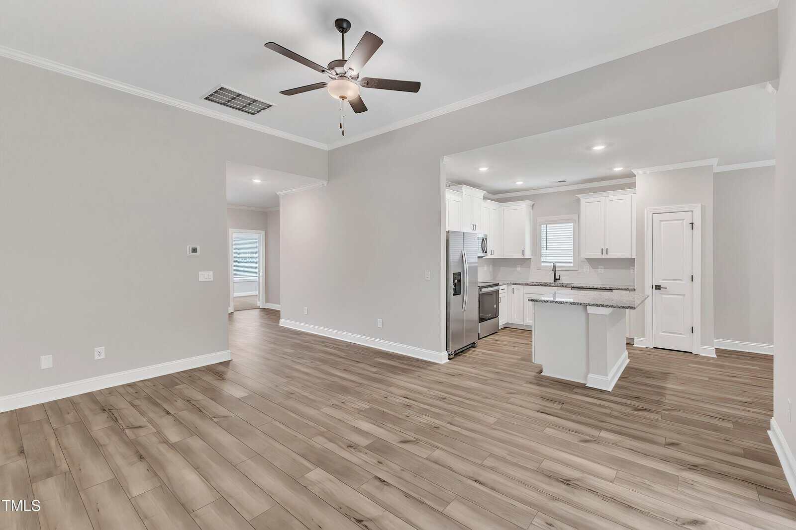 Open-concept living space featuring light wood flooring, neutral walls, a ceiling fan, and recessed lighting. The kitchen has white cabinets, granite countertops, stainless steel appliances, and a central island.