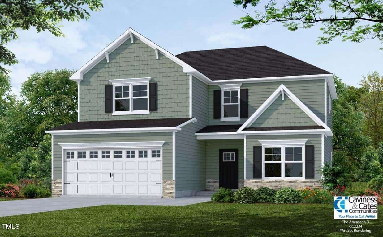 A two-story house with light green siding, white trim, black shutters, and a dark gray roof. It has a double garage, front porch, manicured lawn, and some shrubs. A builder's logo is visible in the bottom right corner.
