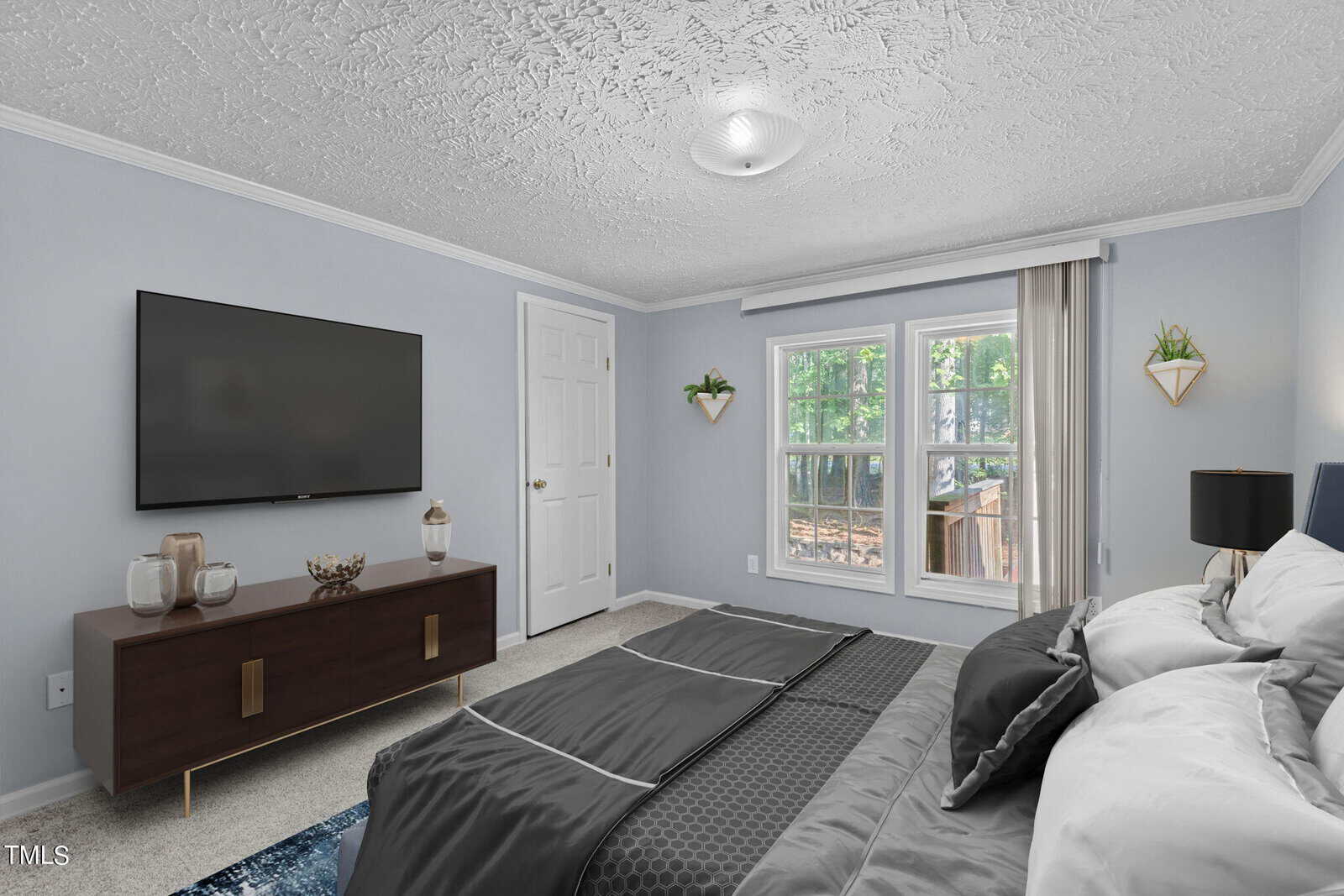 A bedroom with light gray walls, a large bed with dark bedding, a wooden dresser with decor items, a wall-mounted TV, two windows with a view of trees, and two wall planters.