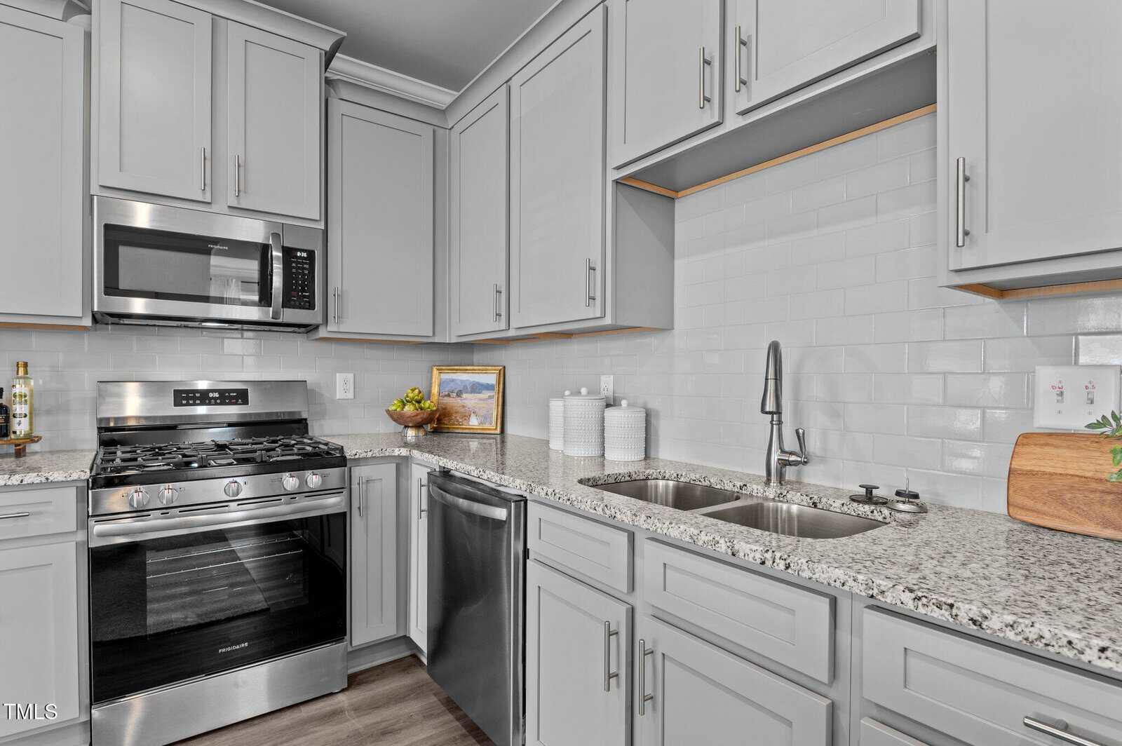 Modern kitchen with light gray cabinets, granite countertops, stainless steel appliances, double sink, gas stove with oven, microwave, dishwasher, tile backsplash, and various kitchen items on the counters.