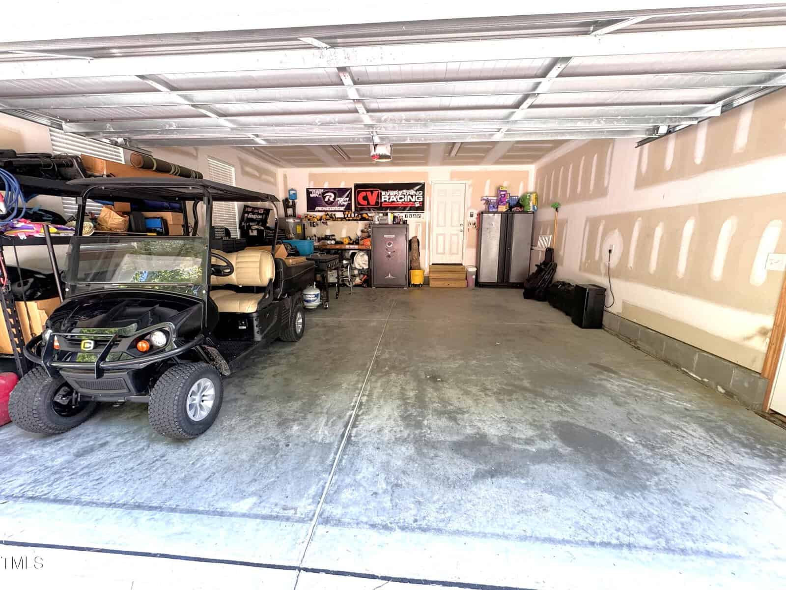 A well-organized garage with a parked golf cart on the left and a variety of items stored along the walls. Shelves hold containers, tools, and boxes. A refrigerator and a steel cabinet are placed against the rear wall. The floor is concrete.