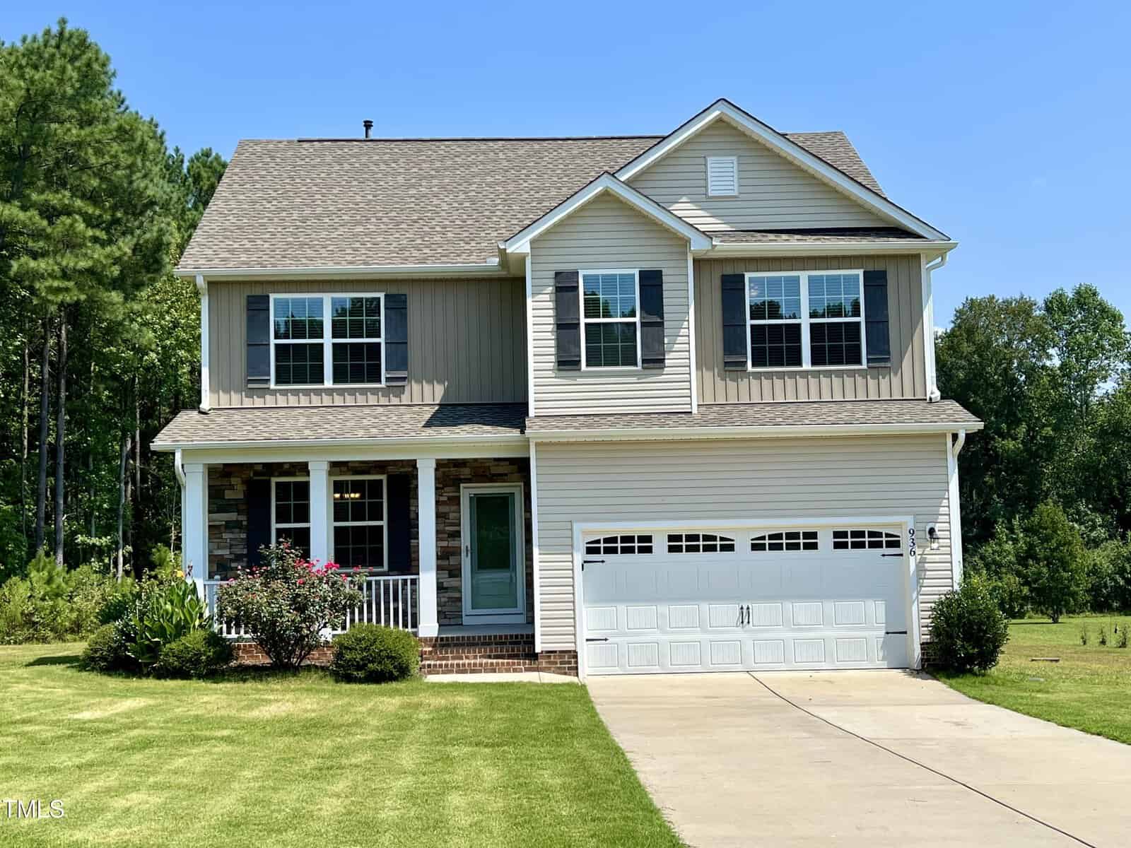 Located at 936 Weatherby Lane, this Creedmoor two-story house boasts a gray and white exterior with a welcoming front porch, numerous windows, and a double garage. A well-kept lawn, shrubs, and trees enhance the serene backdrop under a clear blue sky.