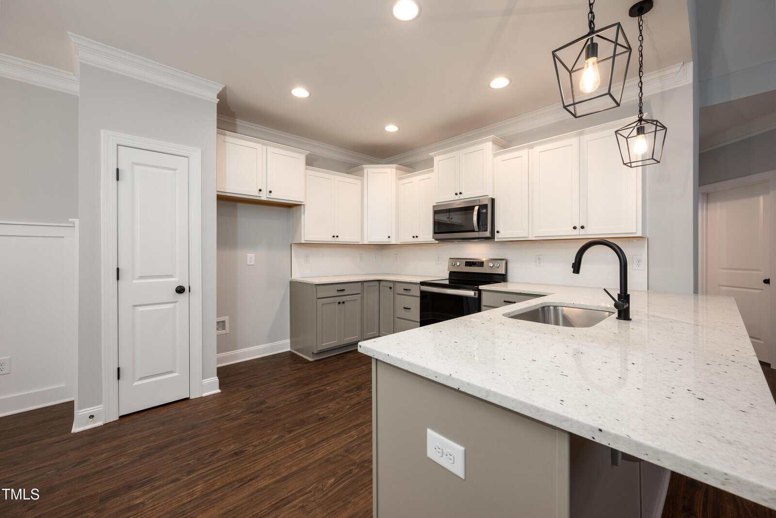 Modern kitchen with white upper cabinets, gray lower cabinets and island, stainless steel appliances, a built-in microwave, dark fixtures, white quartz countertops, pendant lighting, and wood flooring.