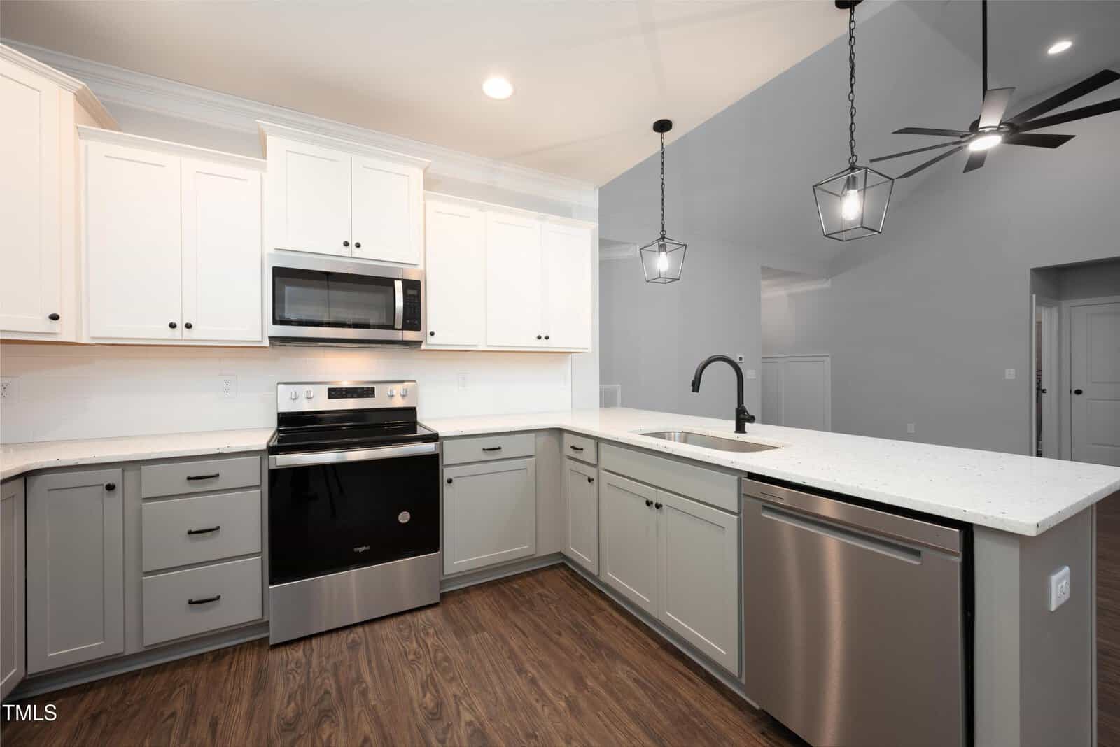 Modern kitchen with white upper cabinets, gray lower cabinets, stainless steel appliances, quartz countertops, a black faucet, pendant lights, and wood flooring. Open layout with high ceilings and neutral walls.