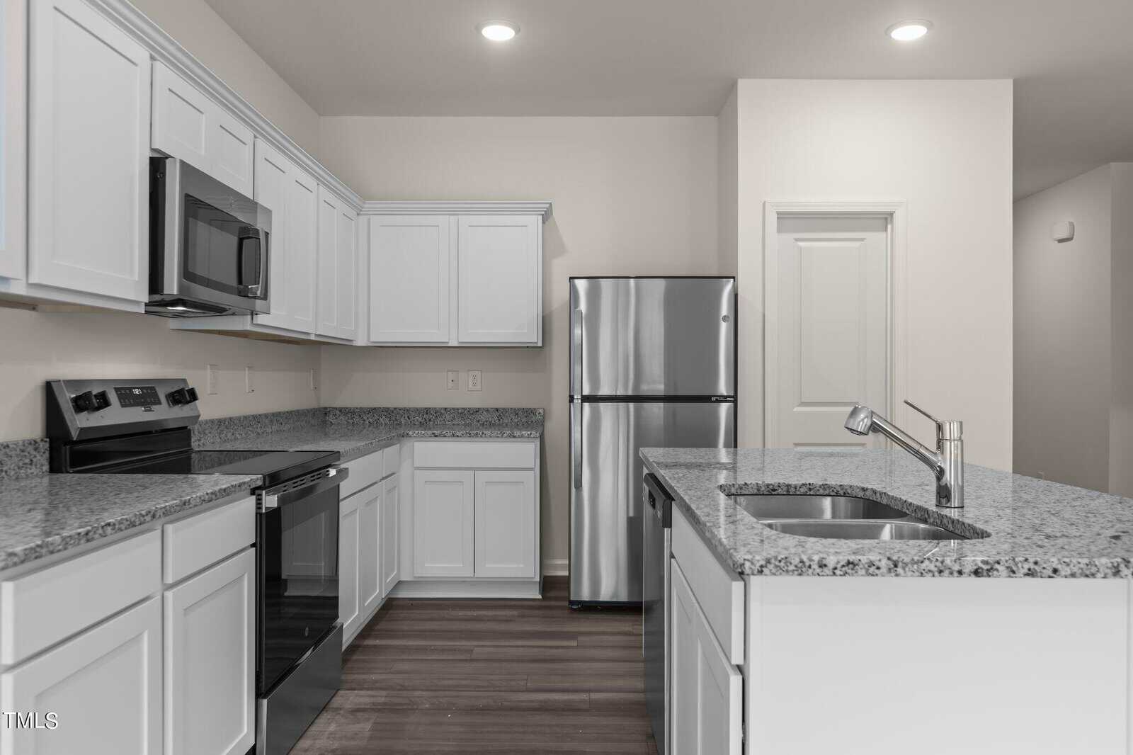 Modern kitchen with white cabinets, stainless steel appliances including a refrigerator, oven, and microwave, granite countertops, an island with a sink, and wood flooring under recessed lighting.