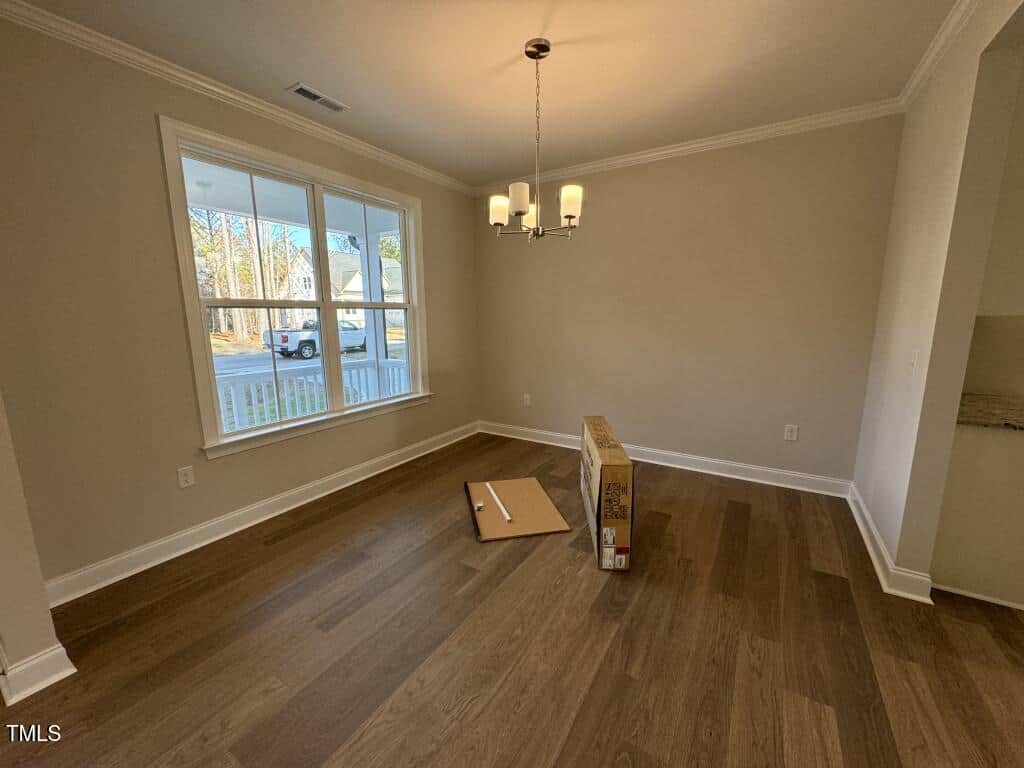 A mostly empty room with light brown wood floors, cream-colored walls, a large window, a modern ceiling light, and an unopened box with scattered packing materials on the floor.