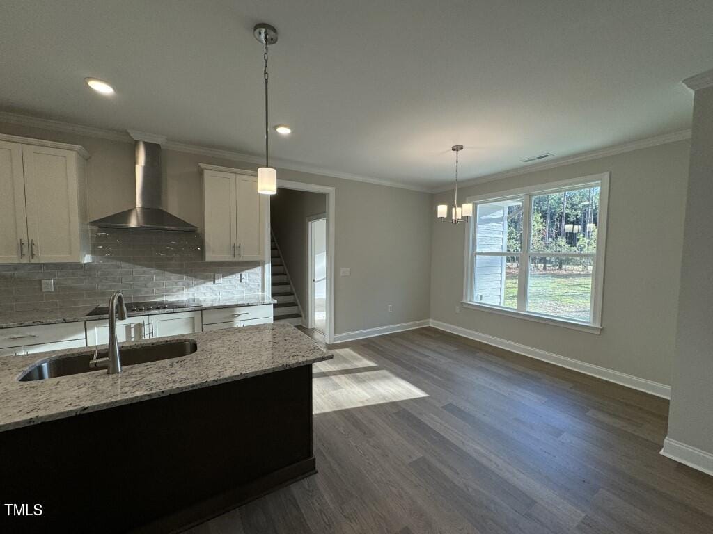 Modern kitchen with island, pendant lights, stainless steel hood, white cabinets, and open dining area. Large window lets in natural light, showing a view of the yard and trees. Staircase visible in the background.