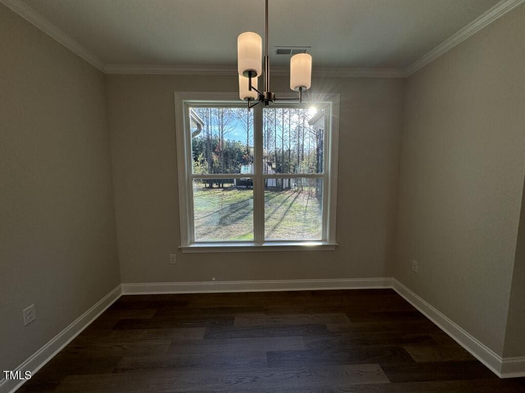 Small empty room with beige walls, dark wood floor, and a double window letting in sunlight. A modern light fixture hangs from the ceiling. Trees and lawn are visible outside the window.