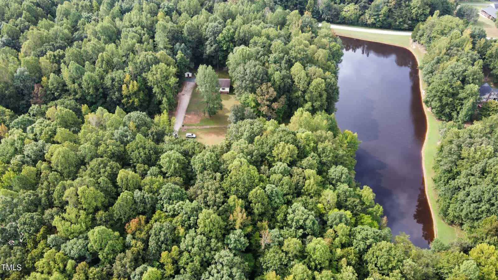 Aerial view of a forested area with a small house and driveway at 1524 Dogwood Drive in the center. A large pond, bordered by trees, is seen on the right near Oxford, with a narrow road running alongside it.