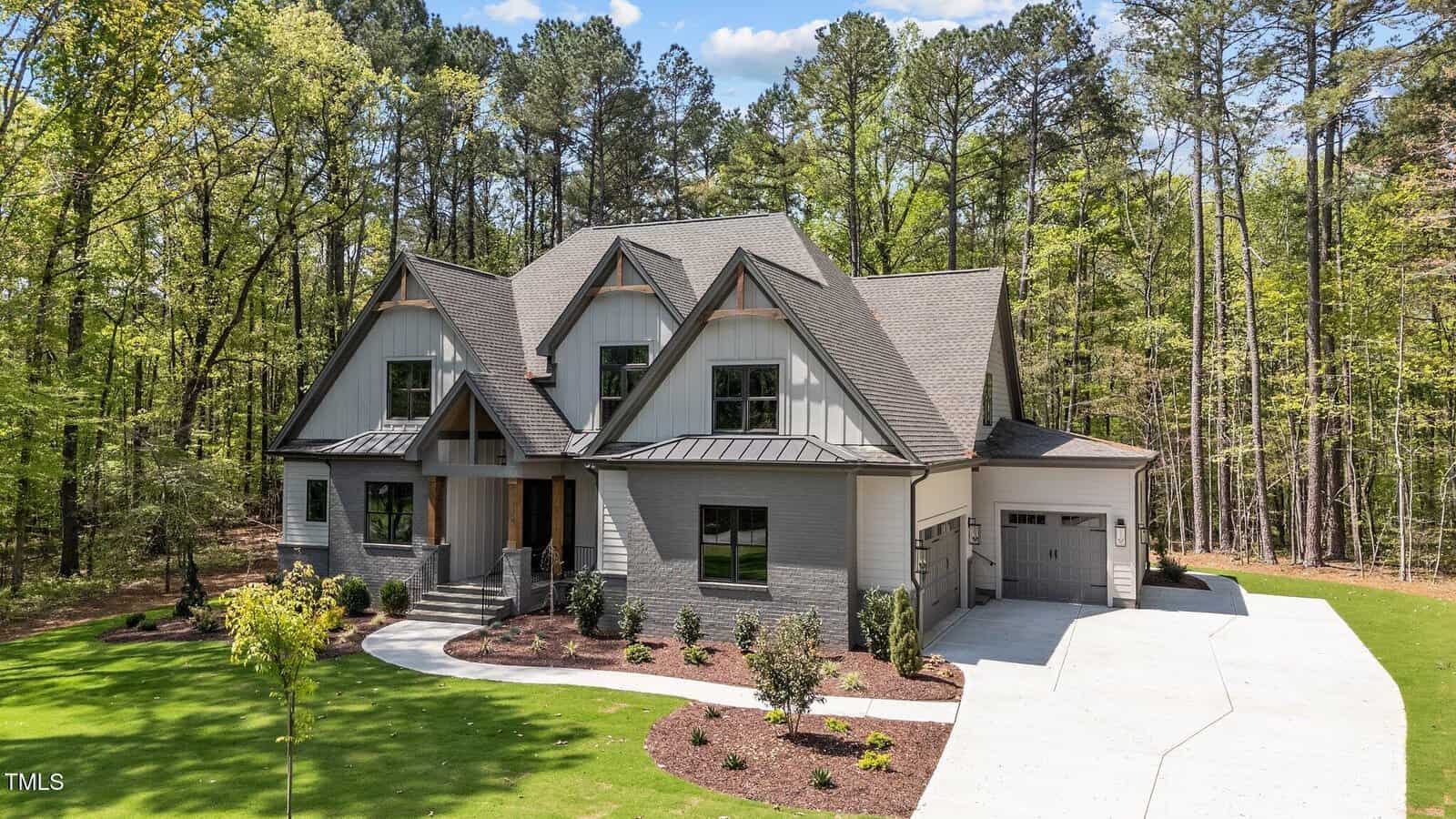 Located at 330 Hidden Lake Drive in Youngsville, this modern two-story house features gray siding, stone accents, a three-car garage, manicured lawn, landscaped plants, and tall trees in the background.