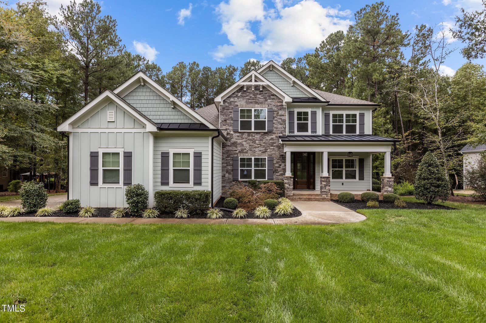 A modern two-story house at 657 Willard Drive features a blend of stone and white siding exterior, surrounded by a well-manicured lawn and shrubs. Nestled in Creedmoor, the home boasts a gabled roof against a backdrop of trees under a partly cloudy sky.