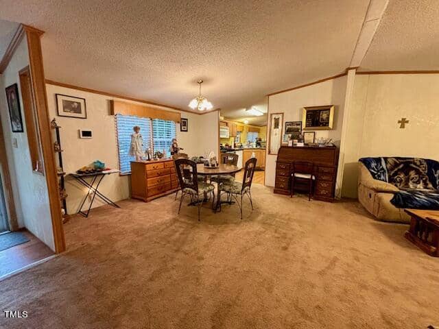 A cozy living and dining area with beige carpet flooring. The dining room has a round table with four chairs. The living room has a couch draped with a blanket featuring a wolf design. Decor includes various framed pictures, a cross on the wall, and wooden furniture.