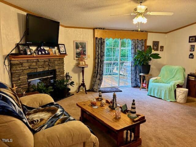 A cozy living room with a fireplace adorned with photos and a folded American flag. A wall-mounted TV is above the mantle. A wooden coffee table decorates the center. There's a green armchair next to sliding glass doors leading to a deck, and another upholstered chair nearby.