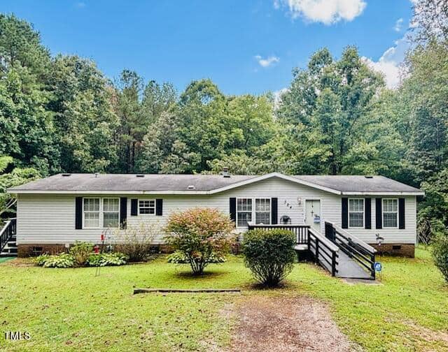Located at 324 Marigold Lane in Henderson, this single-story, white, ranch-style house features a dark roof, black shutters, a front porch, and a ramp leading to the entrance. It is surrounded by greenery, including shrubs and trees, with a grassy lawn in front. The sky above is partly cloudy.