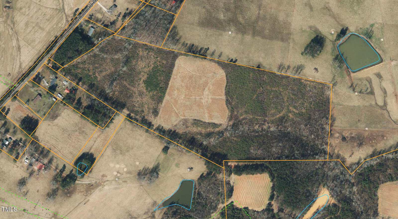 Aerial view of a rural landscape with fields, trees, and several small ponds. The area is divided by lines indicating property boundaries. A large patch of cleared land is visible in the center, surrounded by wooded areas and smaller plots.
