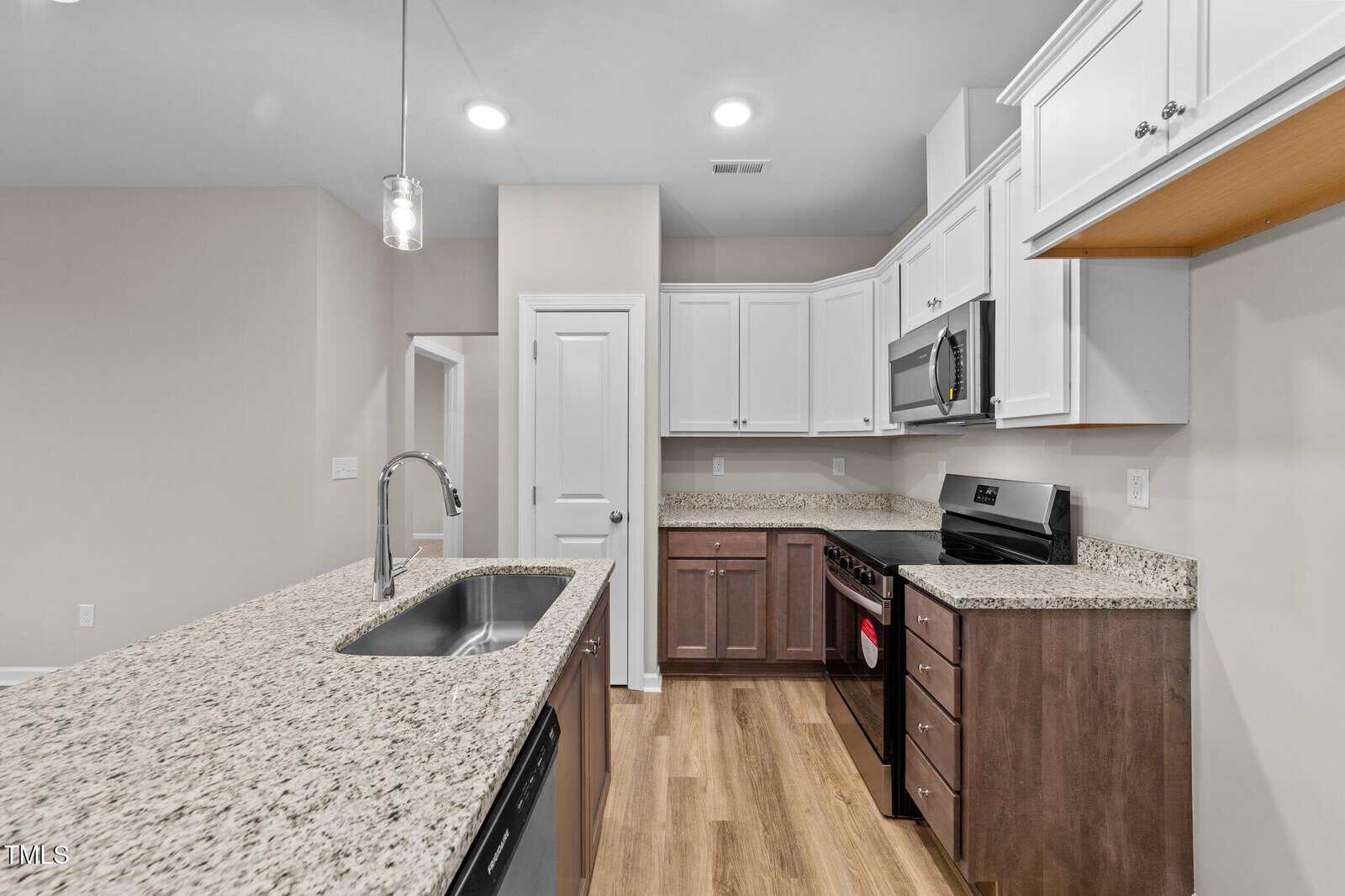 A modern kitchen with granite countertops, stainless steel appliances, white upper cabinets, and dark lower cabinets. There is a center island with a sink and faucet, and wood flooring throughout.