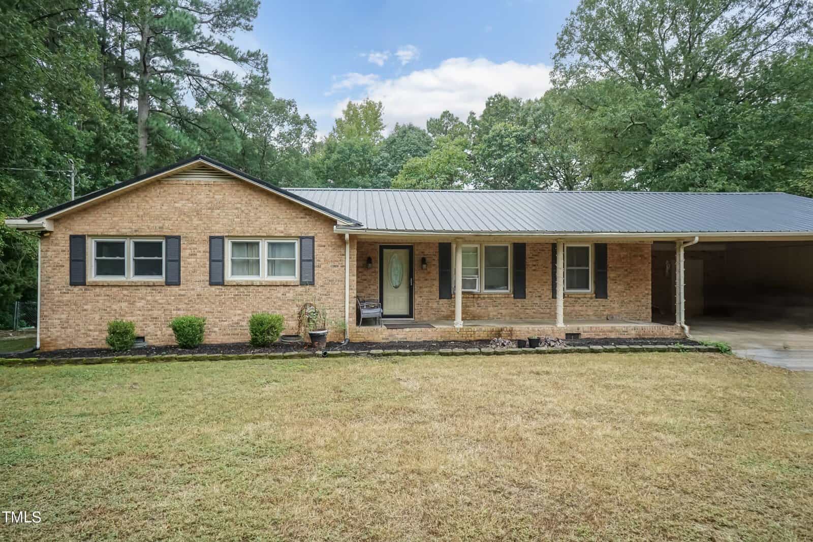 A single-story brick house at 2788 Vicksboro Road with a covered front porch, a glass-paneled front door, and three front-facing windows. The home is surrounded by a neatly mowed lawn, small shrubs, and is situated next to a wooded area in Henderson. An attached carport is on the right side.