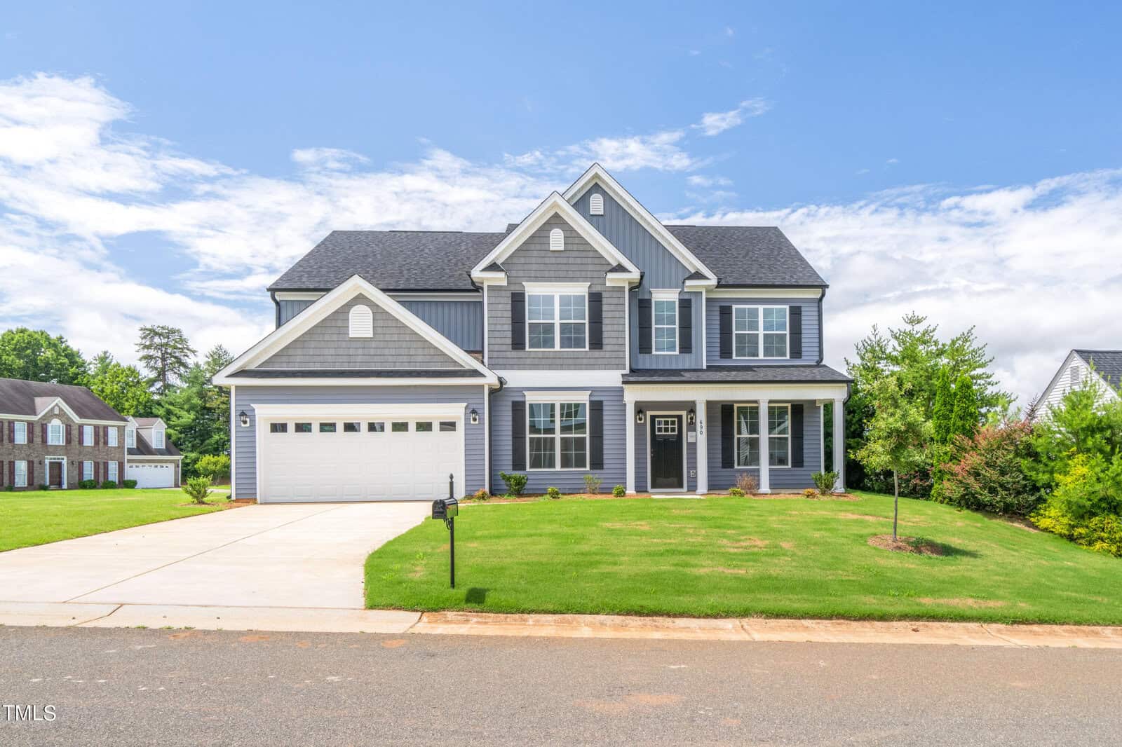 A two-story gray suburban house with white trim, a double garage, covered front porch, and manicured lawn, set under a blue sky with some clouds.
