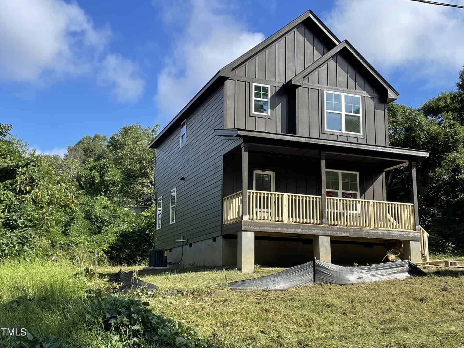 Nestled on a grassy slope, the modern two-story house at 509 Grant Street in Henderson boasts dark gray siding and a charming covered front porch. Wooden railings frame the porch, inviting you to relax amid lush greenery and trees under a partly cloudy sky.