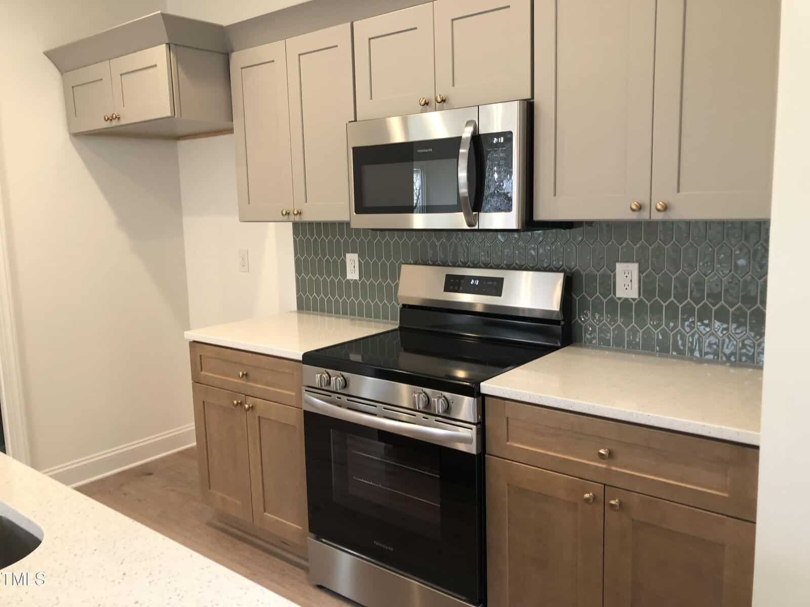 Modern kitchen with beige and gray cabinets, a stainless steel oven and microwave, white countertops, and a textured green tile backsplash. The floor is light brown wood.