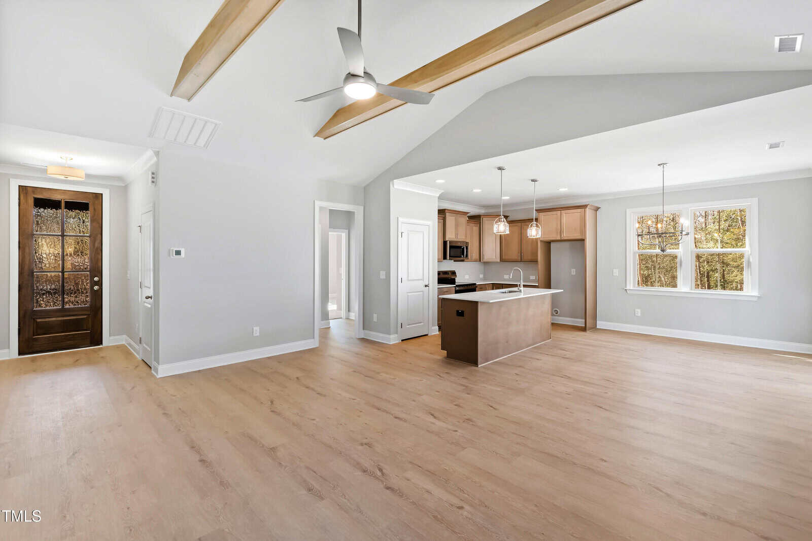 Open-concept living area featuring light wood flooring, exposed ceiling beams, ceiling fans, and a modern kitchen with an island, stainless steel appliances, light wood cabinets, and large windows letting in natural light.
