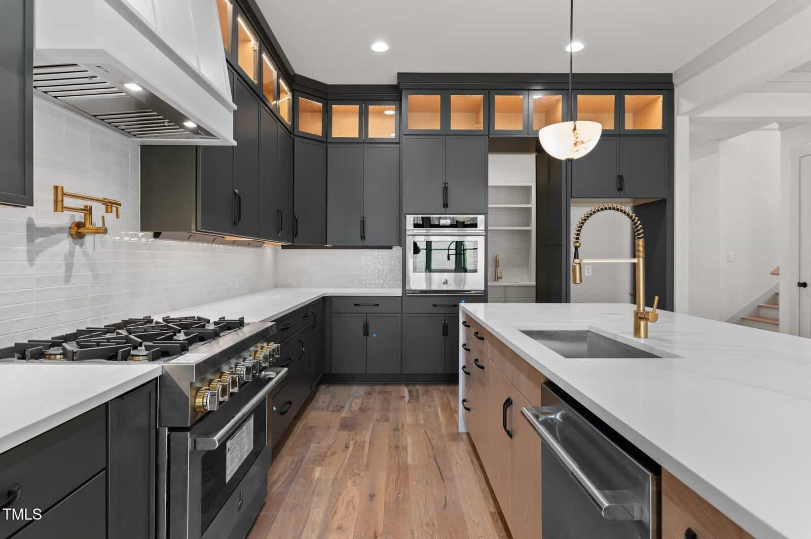 Modern kitchen with dark cabinets, white countertops, stainless steel appliances, a gas stove, double wall oven, open shelving, a gold faucet, and a wood floor. A walk-in pantry is visible in the background.