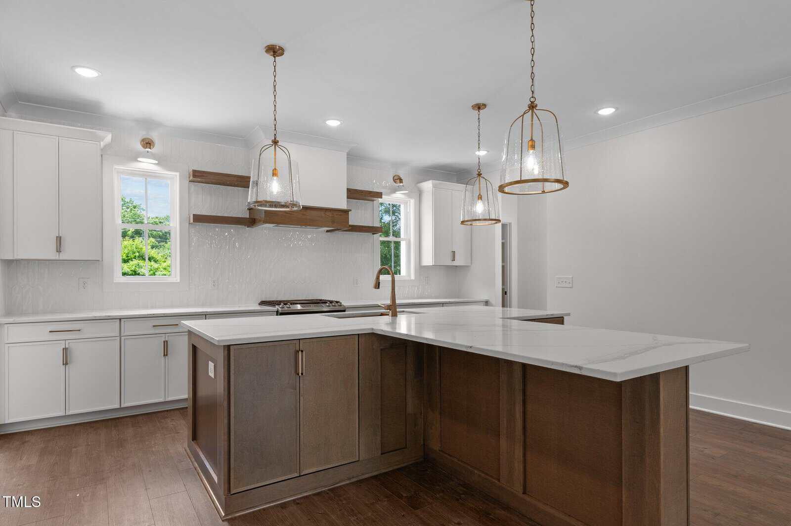 Modern kitchen with white cabinets, brown island with marble countertop, three pendant lights, wood floors, two windows, open wood shelves, and a built-in stove with a white backsplash.