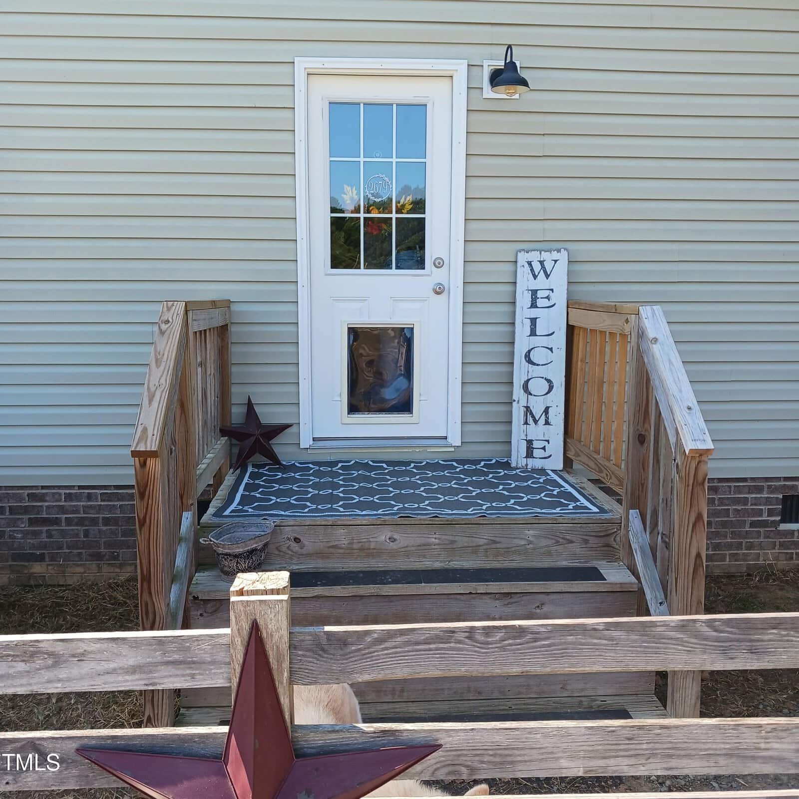 A small wooden porch with a "Welcome" sign leads to a door with a glass window. A dog sits behind the door, looking out. A large red star decorates the lower foreground, and a small star is on the porch.